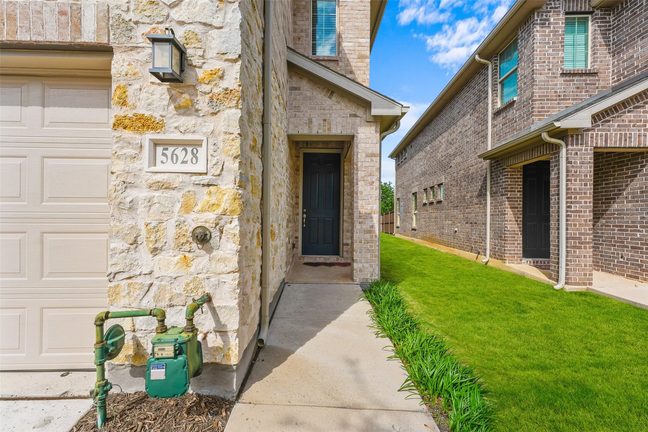 Stone and brick exterior featuring an attached garage with a panel door, a black entry door, and a concrete pathway