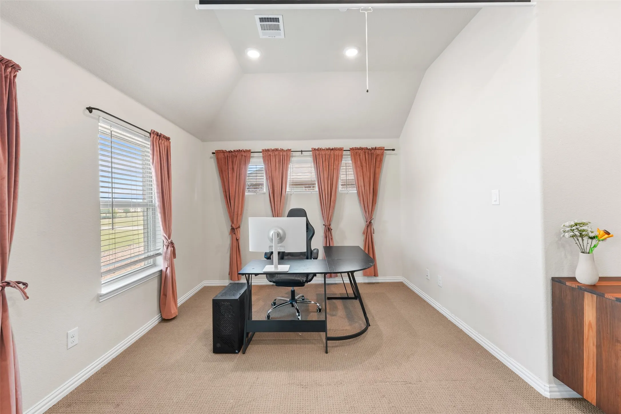 Carpeted room featuring multiple windows with blinds, a vaulted ceiling, and recessed lighting