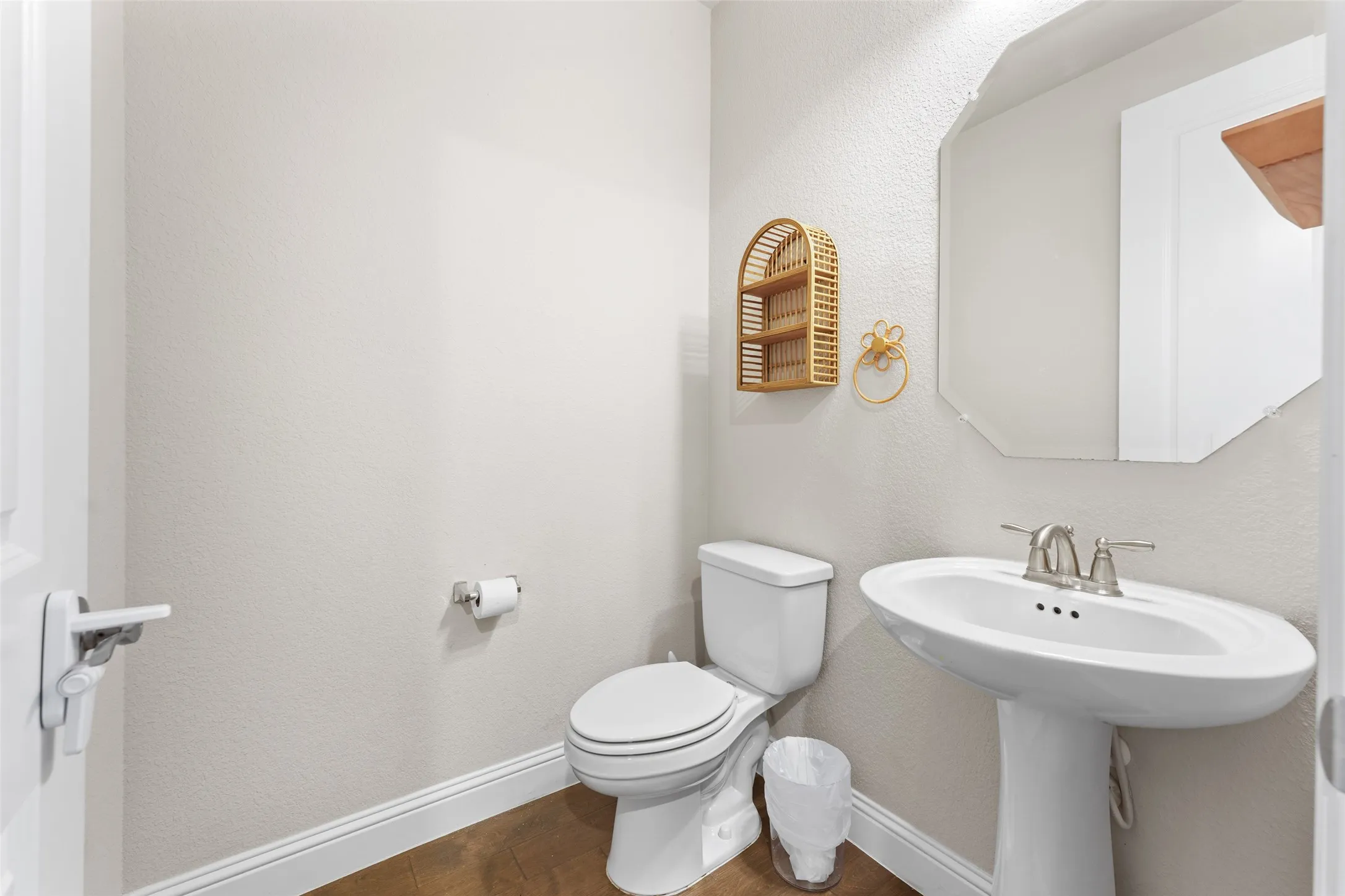 Bathroom featuring a pedestal sink with a brushed nickel faucet, a two-piece toilet, wood-finish flooring, and a wall-mounted octagonal mirror