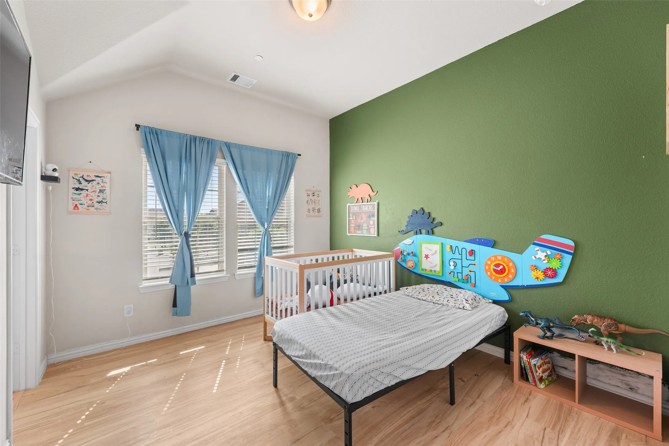 Room featuring vaulted ceilings, light wood-finish flooring, and two windows with blinds