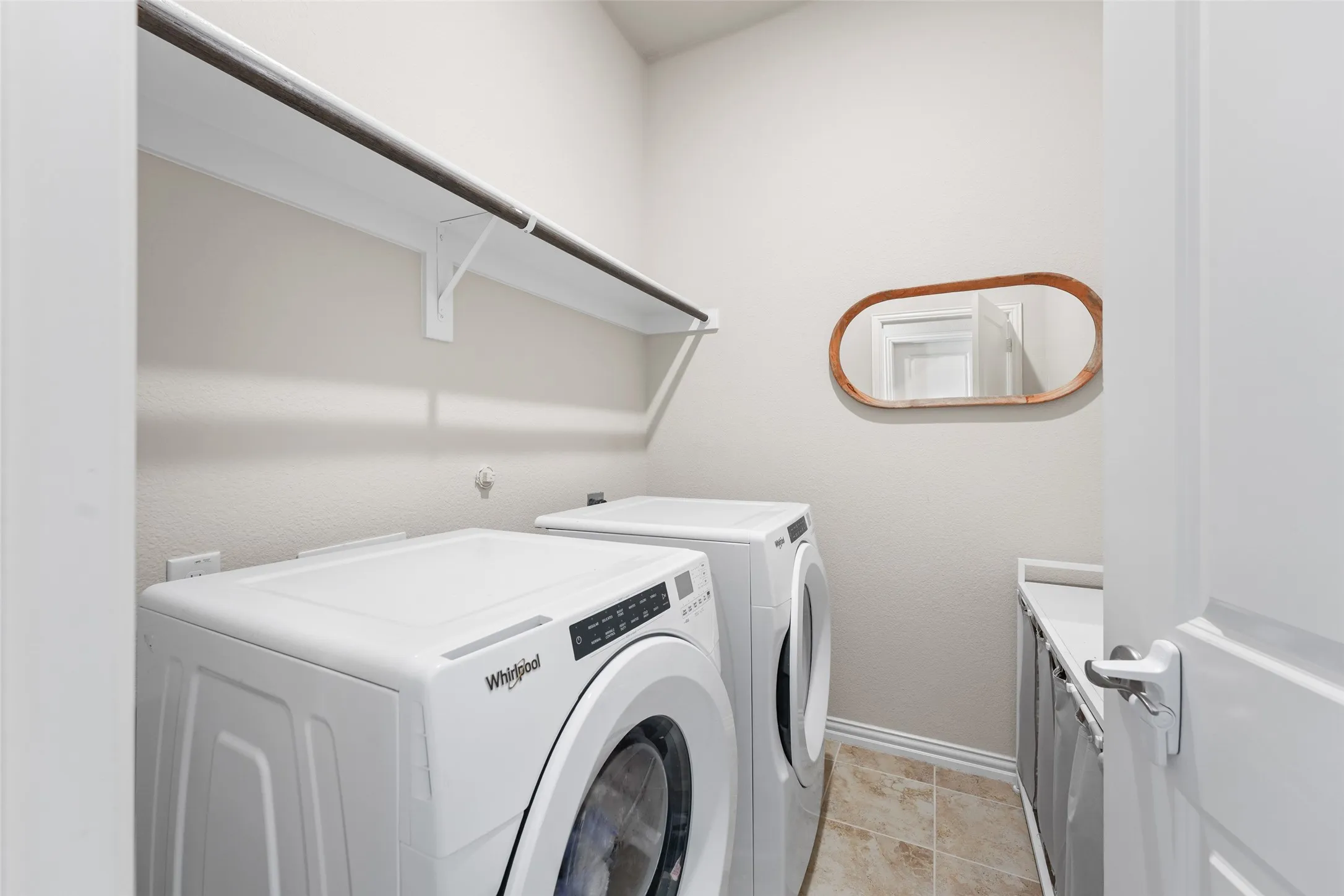 Dedicated laundry space featuring a white shelf with a hanging rod, tile flooring, and light-toned walls
