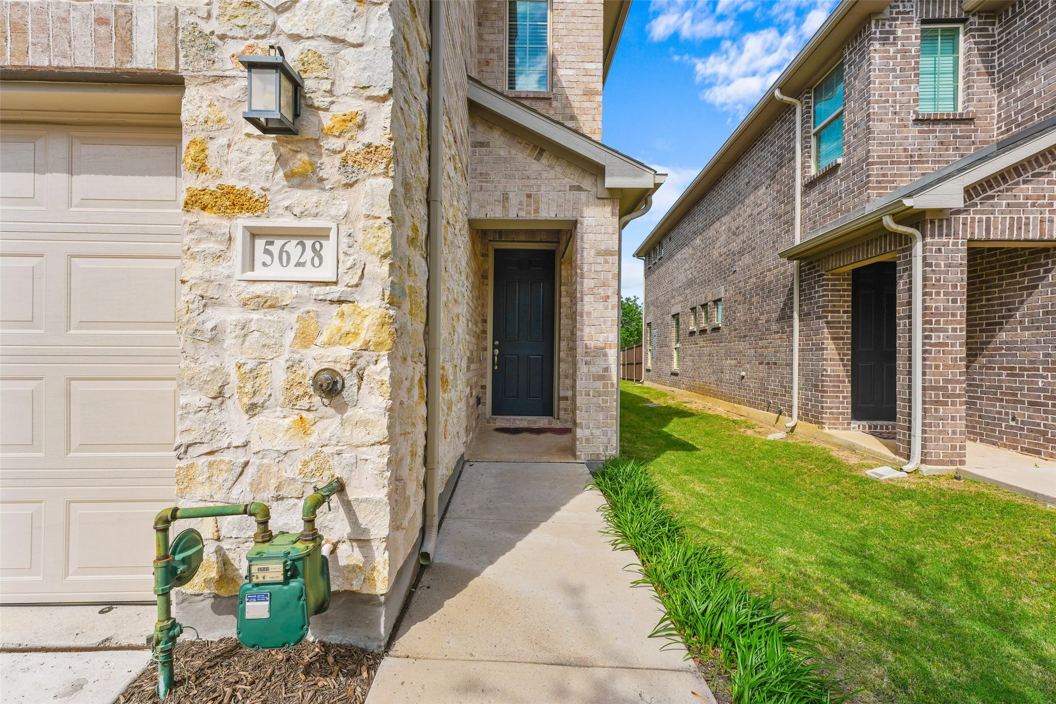Stone facade entry with a dark paneled front door, covered porch, and exterior sconce lighting