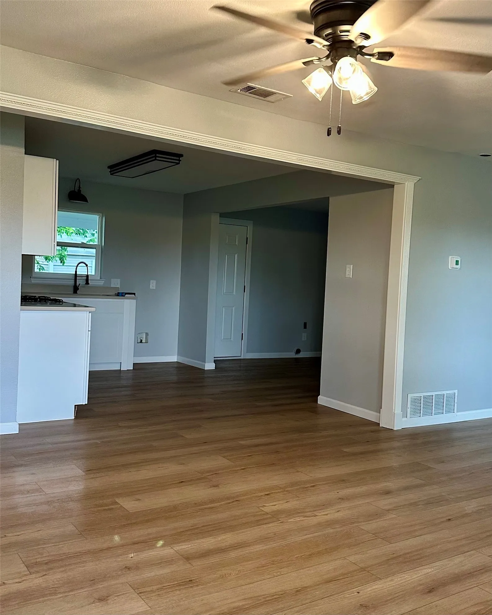 Wood-finish flooring throughout, white baseboards, and a modern ceiling fan with integrated lighting