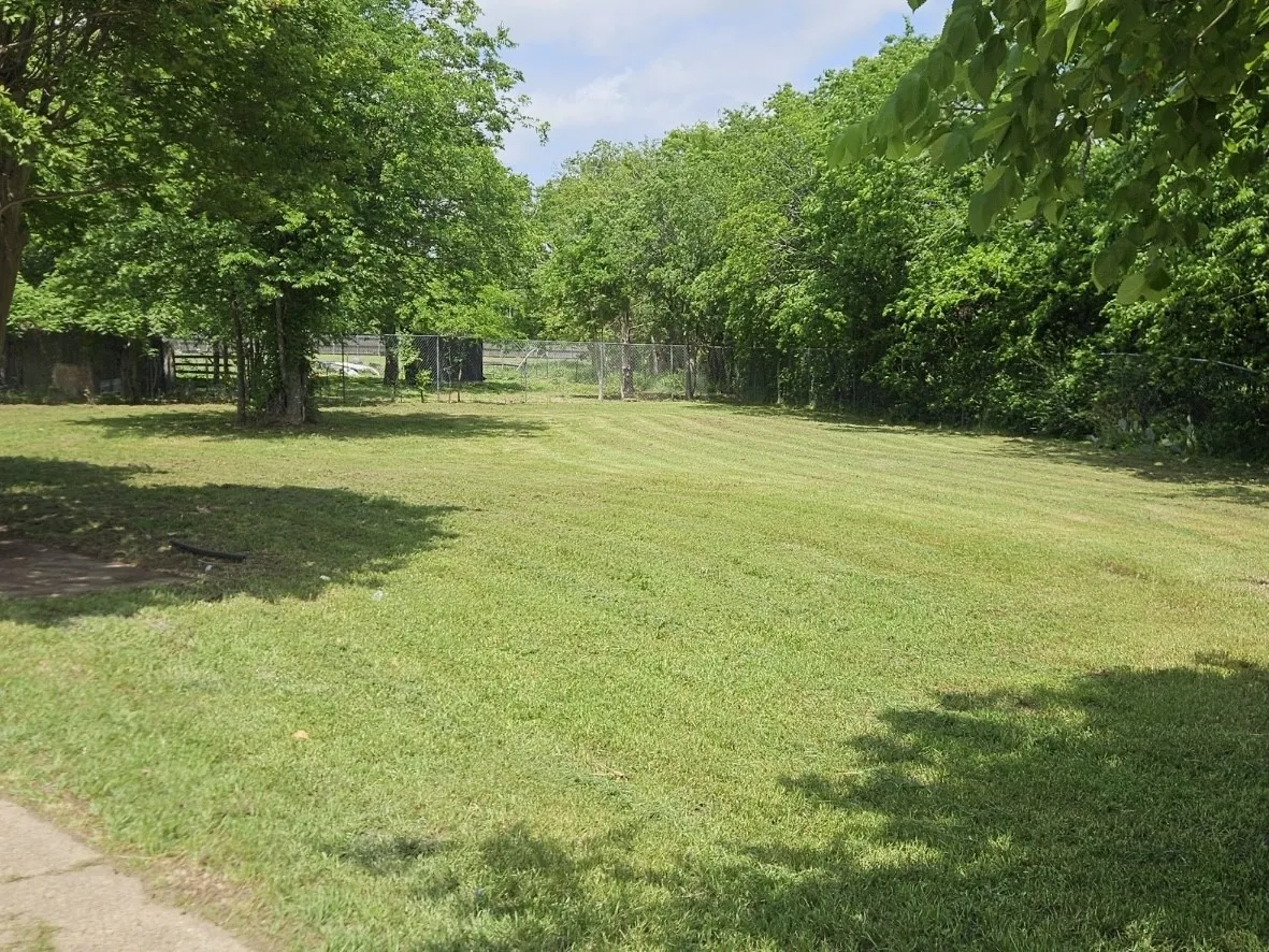 Expansive grassy area featuring mature trees and partial fencing