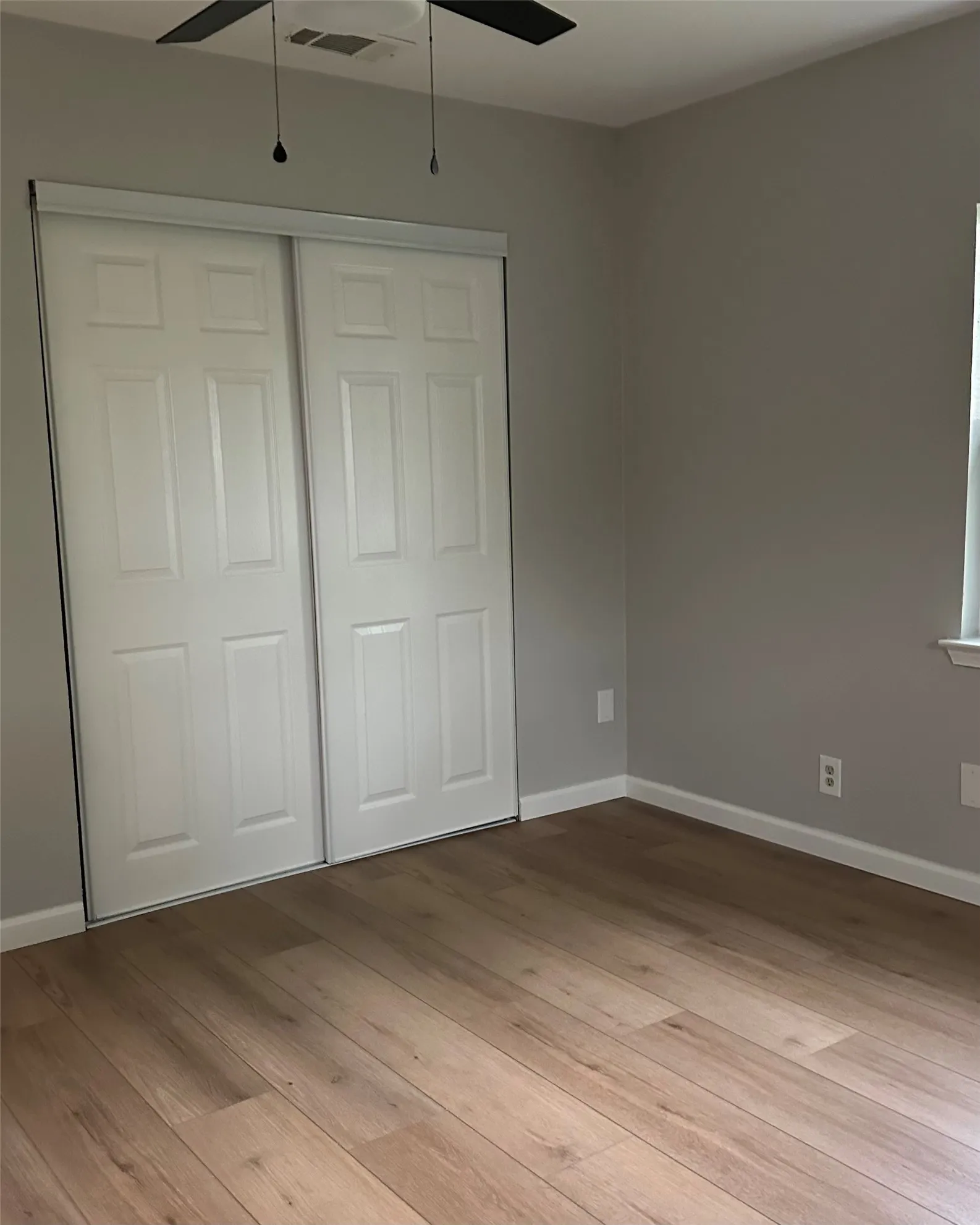 Wood-finish flooring, sliding panel closet doors, ceiling fan with lighting, and neutral wall tones