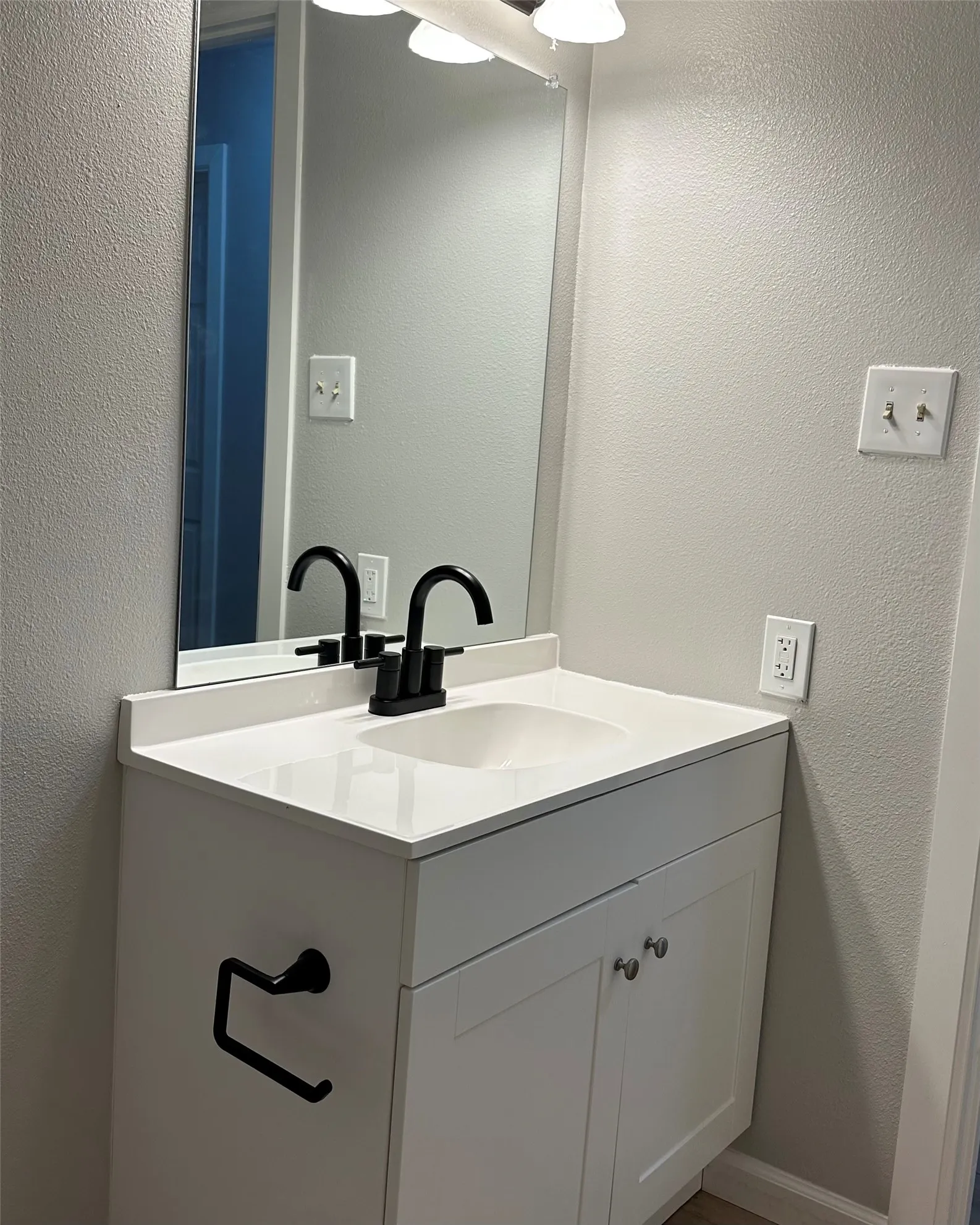 White vanity with a white countertop and integrated sink, matte black faucet, and frameless mirror