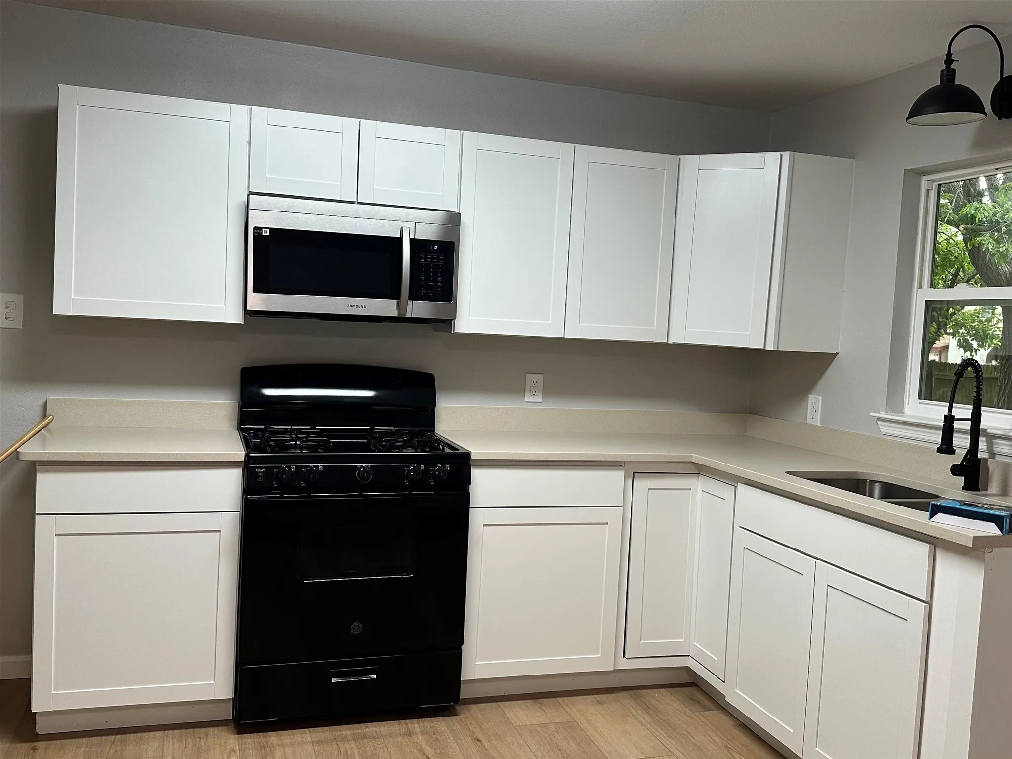 White shaker cabinetry, light-toned countertops, stainless steel microwave, black range, and wood-finish flooring