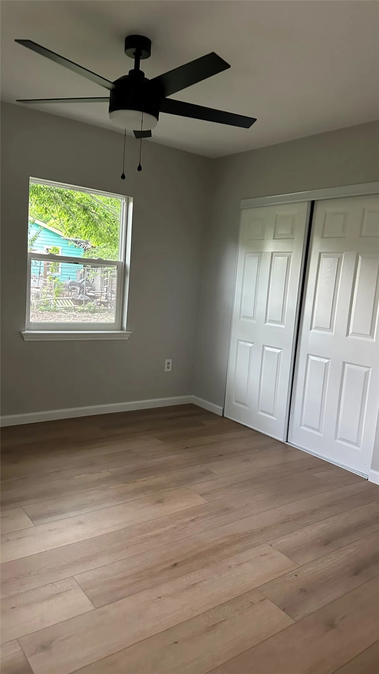 Wood-finish flooring, white bi-fold closet doors, ceiling fan with integrated lighting, and a single window
