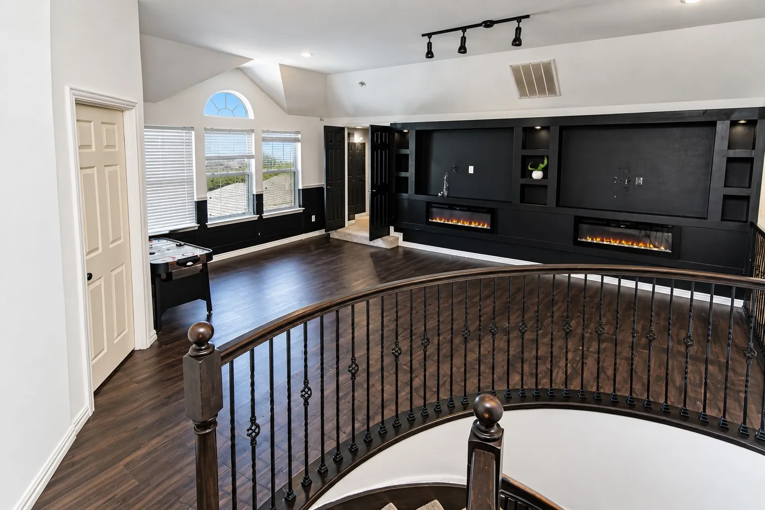 Open-concept room featuring wood-finish flooring, a built-in media console with two electric fireplaces, and multiple windows with an arched transom