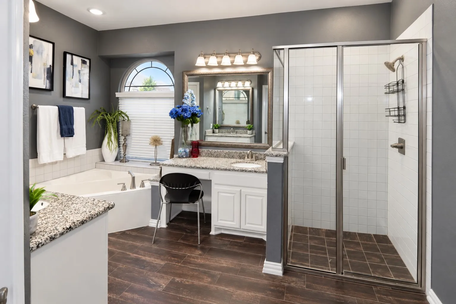 Spacious master bathroom featuring a corner soaking tub, a walk-in shower with a glass enclosure, wood-finish flooring, and a vanity with a granular countertop