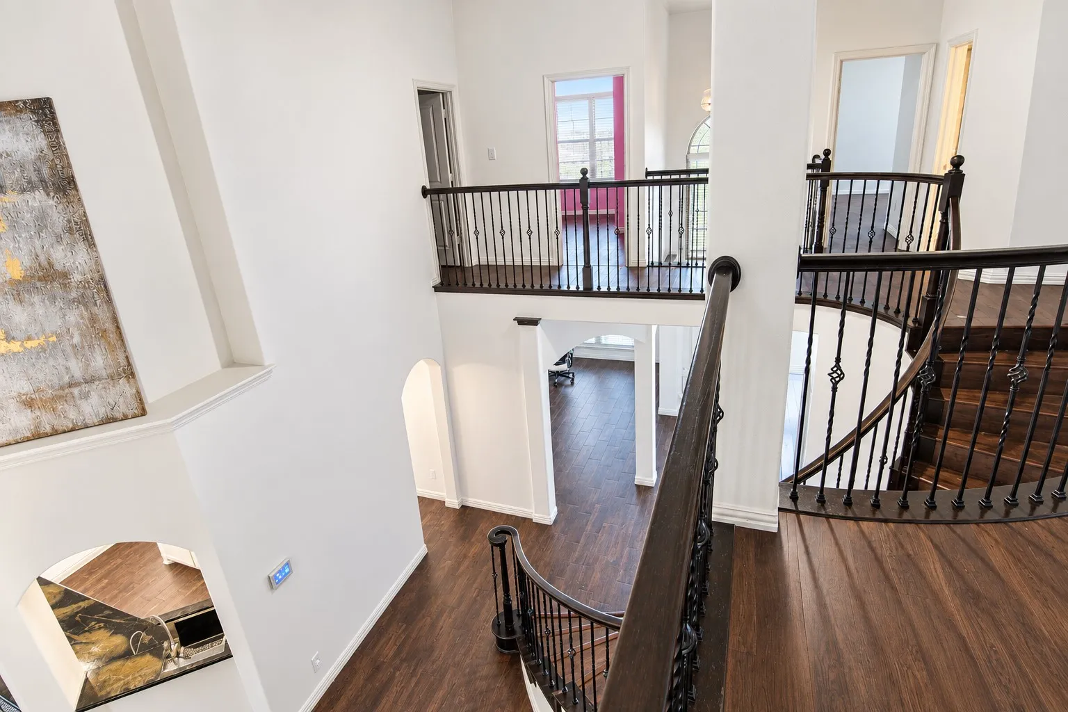 Wood-finish flooring throughout, wrought iron balusters, arched doorways, and upper-level landing