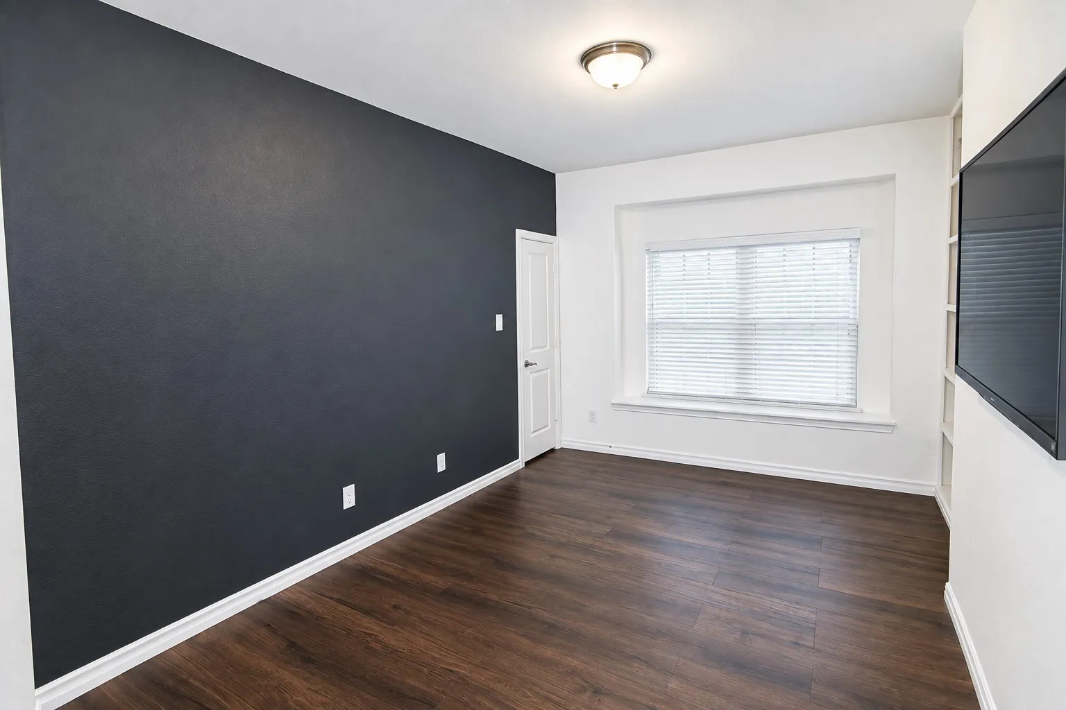 Wood-finish flooring, accent wall, built-in shelving, window with blinds, and flush mount lighting