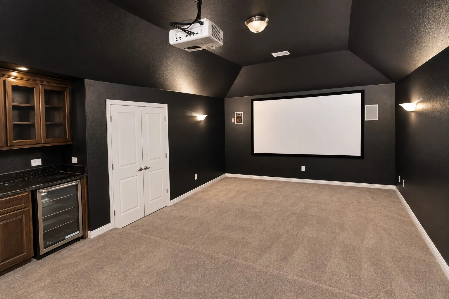 Dedicated media room featuring a large projection screen, built-in dry bar with granite countertop, integrated beverage refrigerator, and recessed lighting