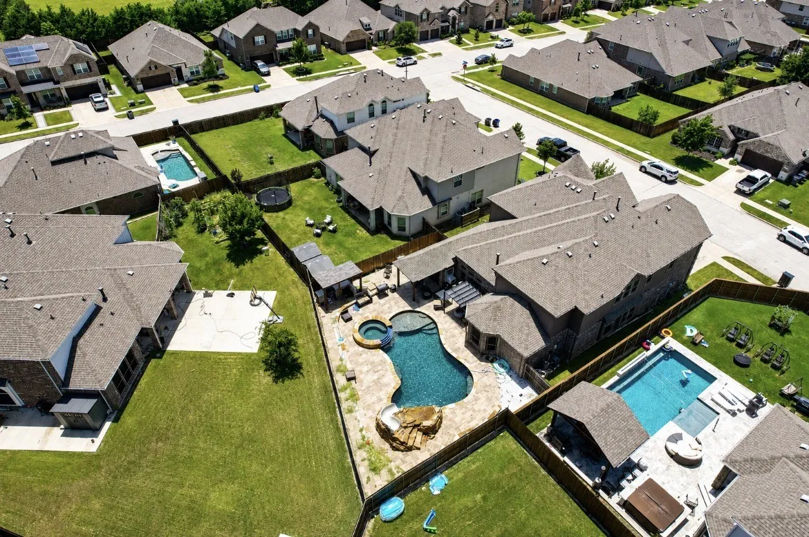 Aerial perspective of a residential neighborhood featuring multiple homes with shingle roofs and fenced backyards