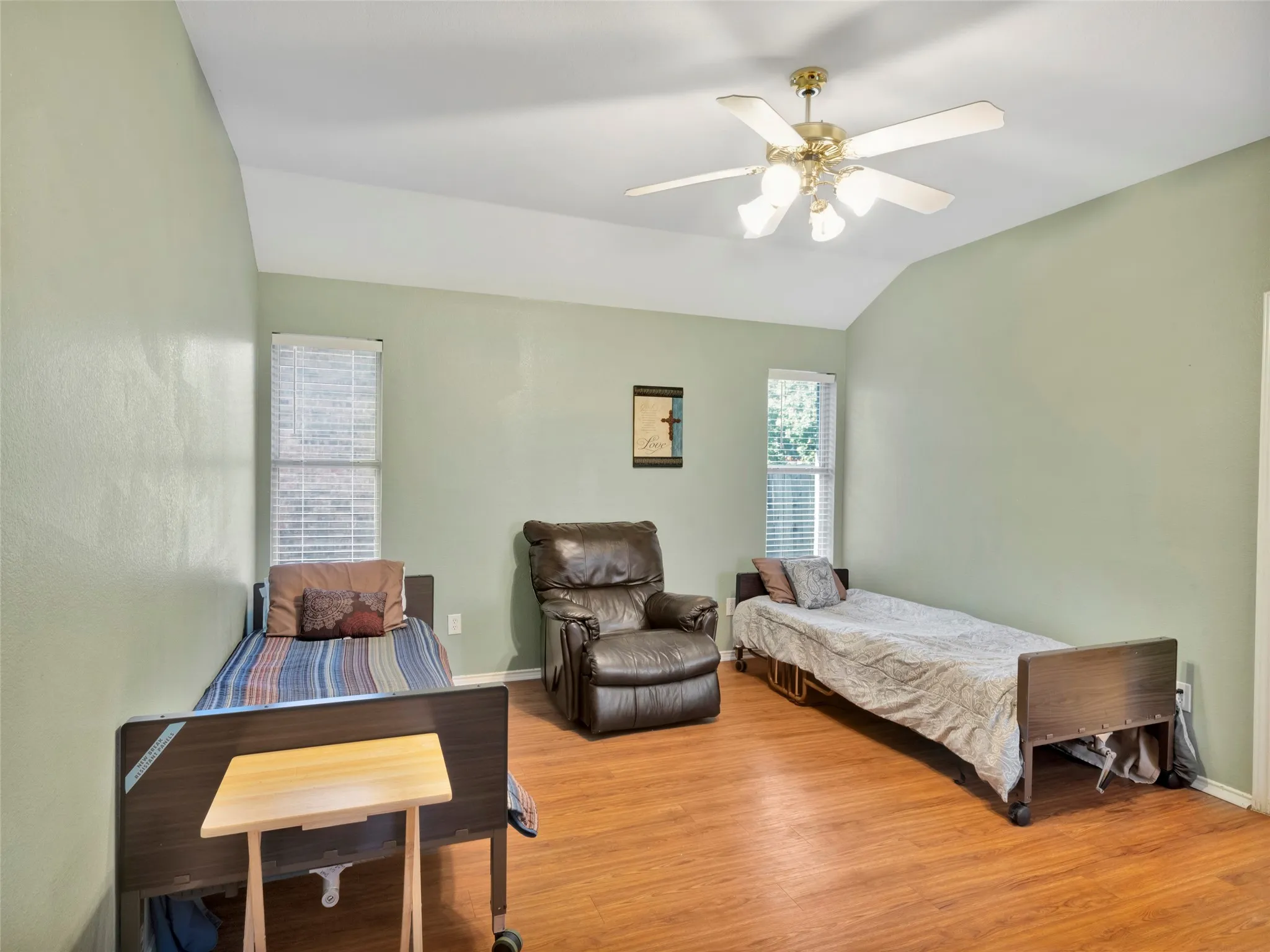 Vaulted ceiling with a ceiling fan, two tall windows with blinds, and wood-finish flooring