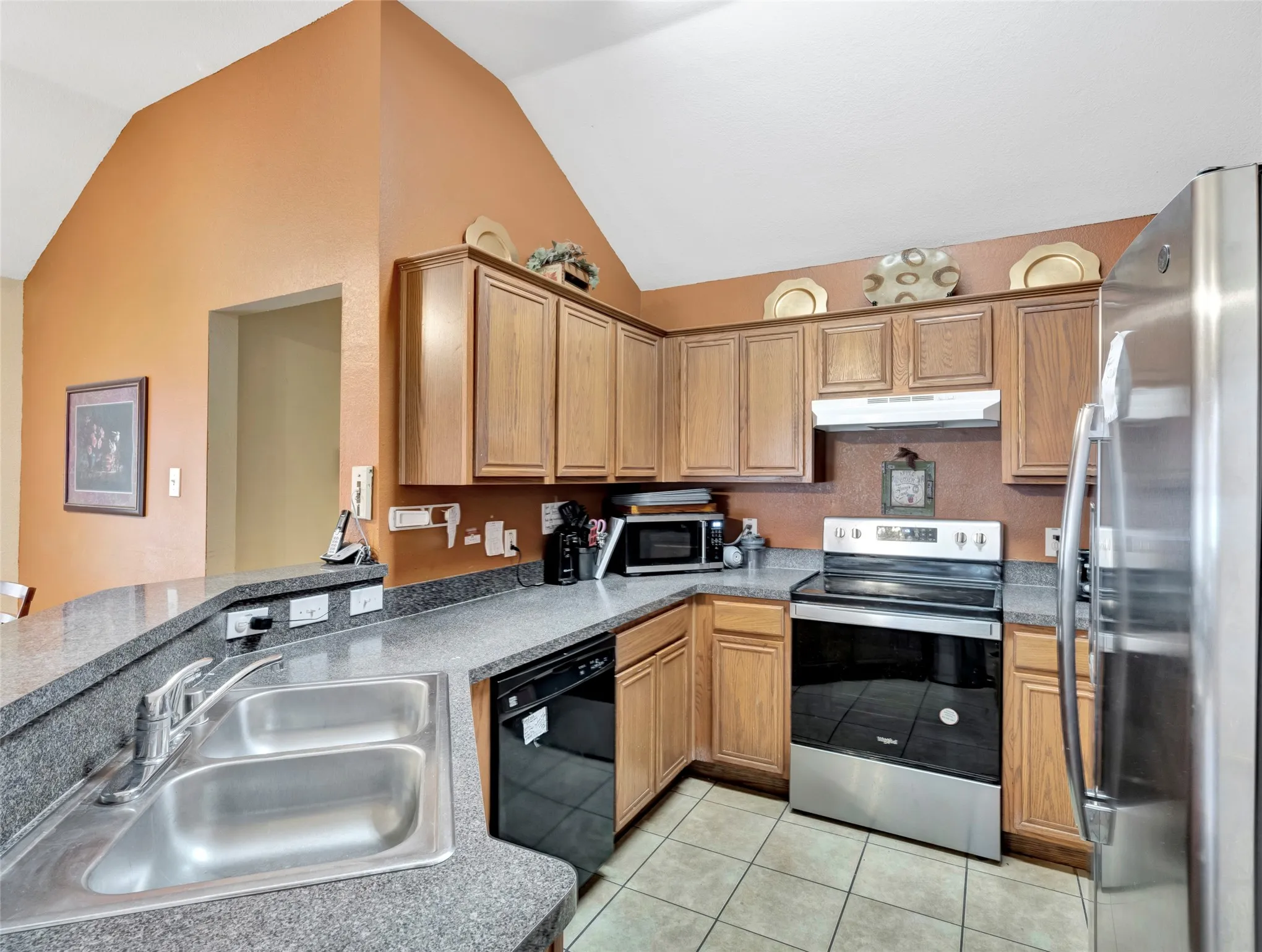Kitchen featuring vaulted ceilings, wood cabinetry, stainless steel appliances, a double basin sink, and tile flooring
