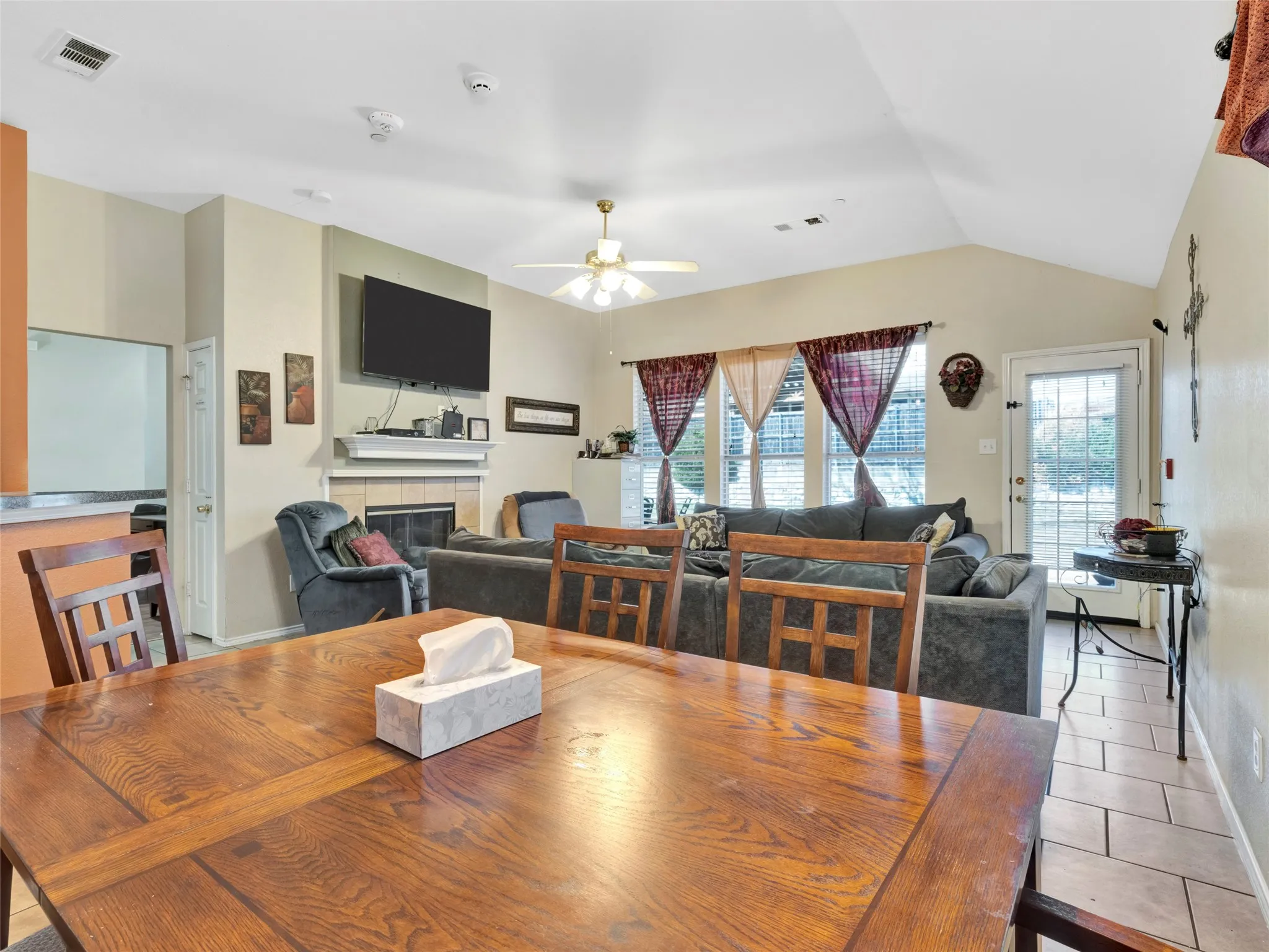 Vaulted ceiling with ceiling fan, fireplace with mantel, tiled flooring, and multiple windows