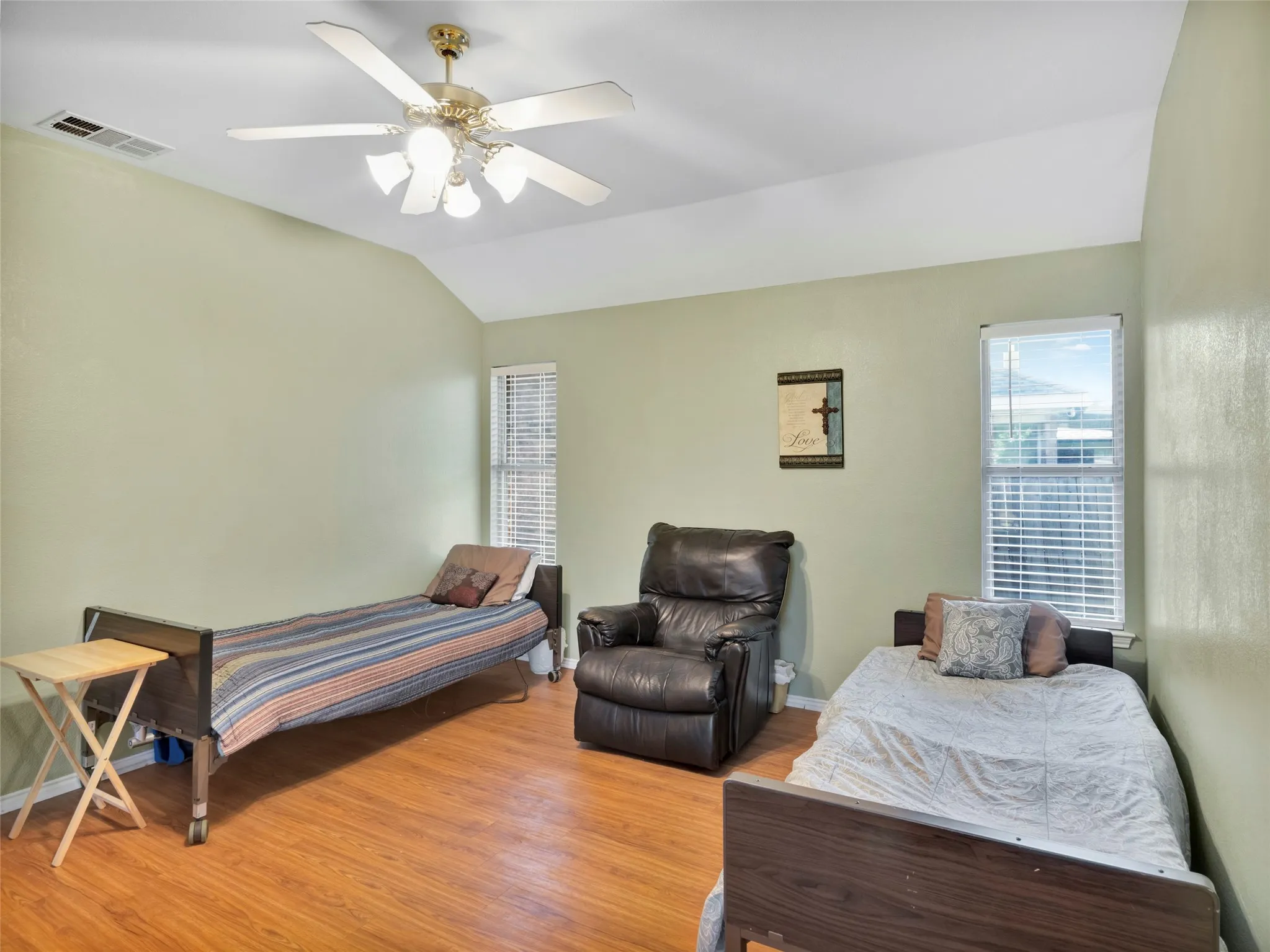 Vaulted ceiling with a ceiling fan, two windows with blinds, and wood-finish flooring