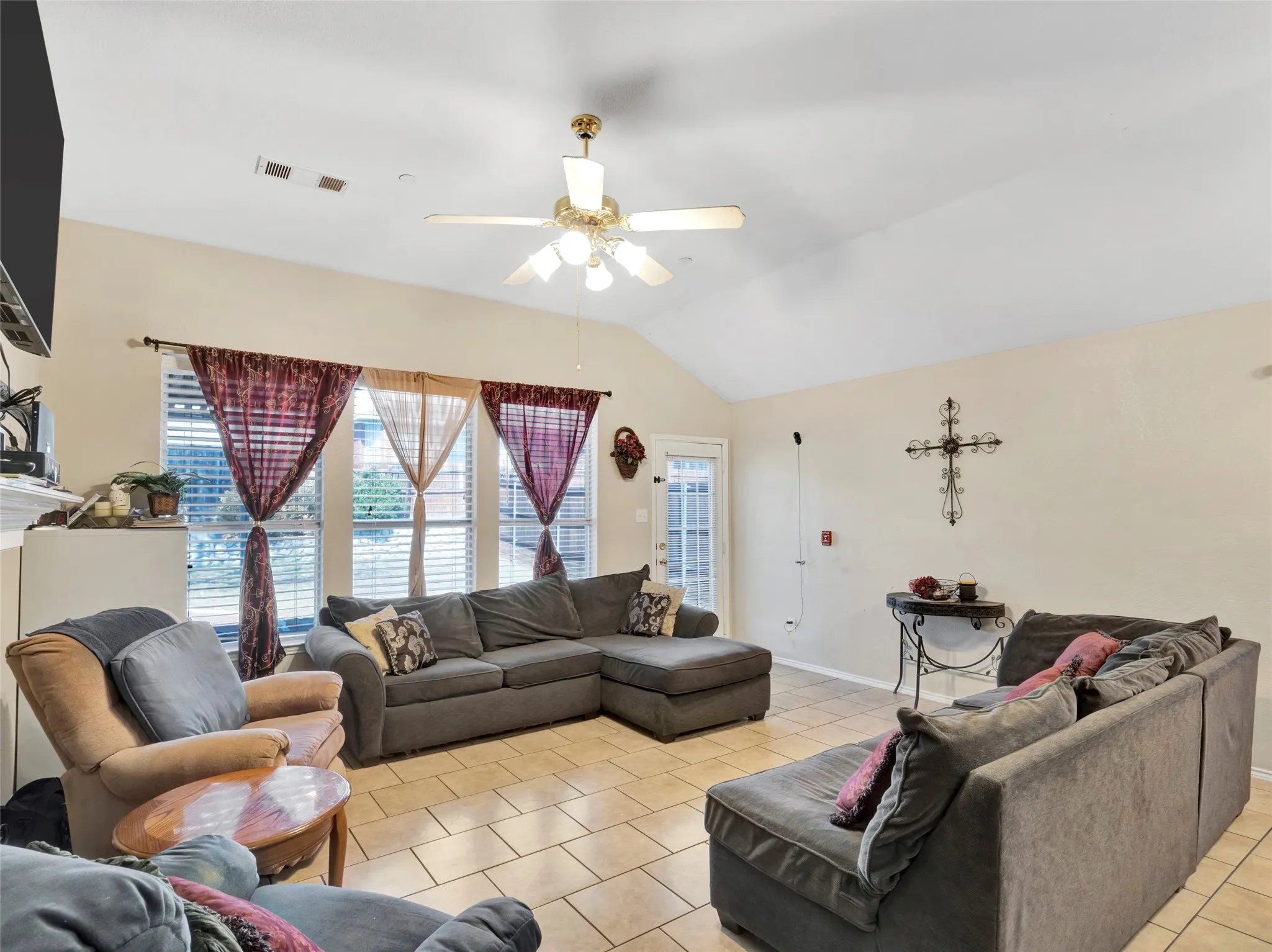 Vaulted ceiling with ceiling fan, ceramic tile flooring, multiple windows, and a glass-paneled door
