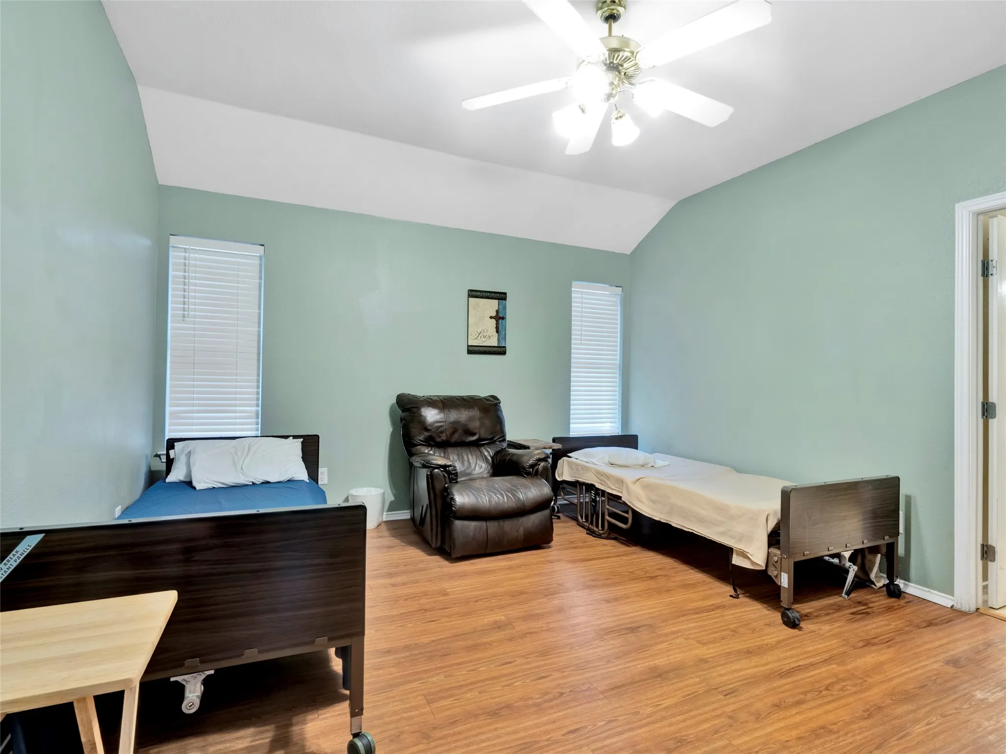 Vaulted ceiling with a ceiling fan light fixture, wood-finish flooring, and two vertical windows with blinds