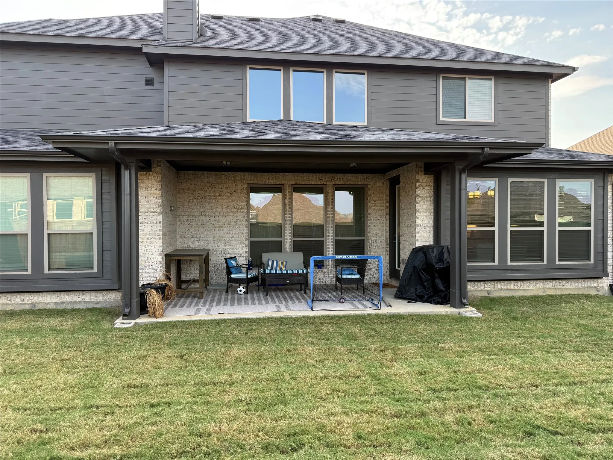 Rear exterior featuring a covered patio with a patterned concrete surface, light brick accents, and dark siding