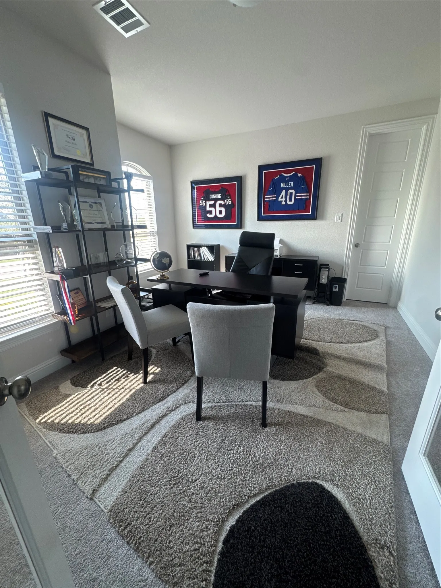 Carpeted room featuring a large area rug with a geometric pattern, multiple windows with blinds, a tall ceiling, and a paneled door