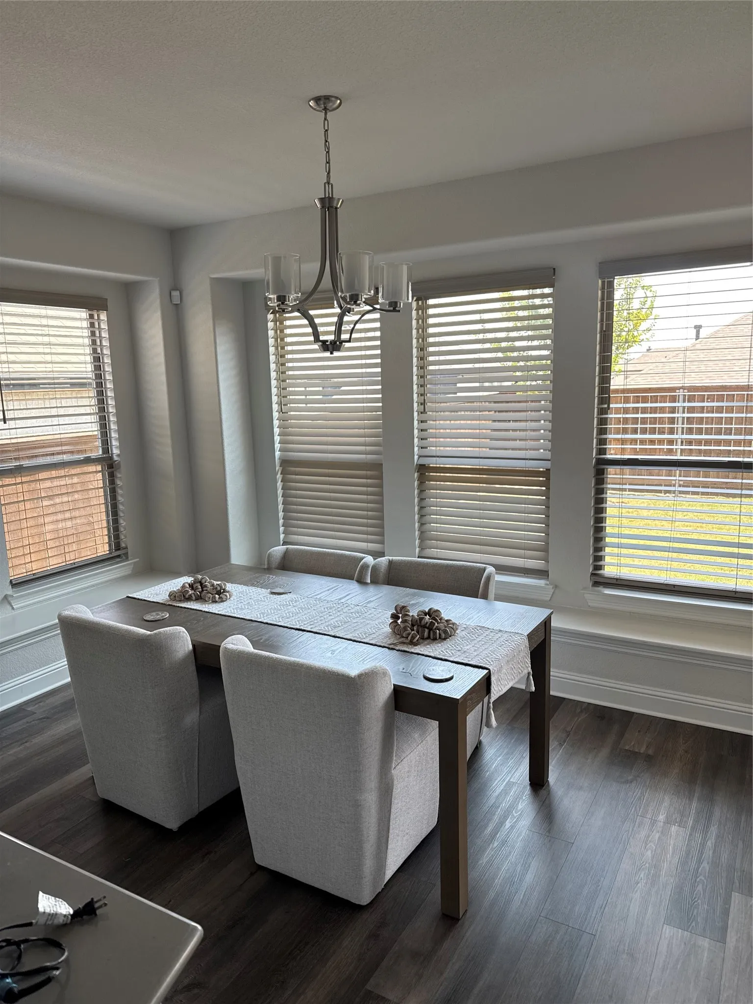 Dining area featuring wood-finish flooring, a contemporary chandelier, multiple windows with blinds, and white baseboards