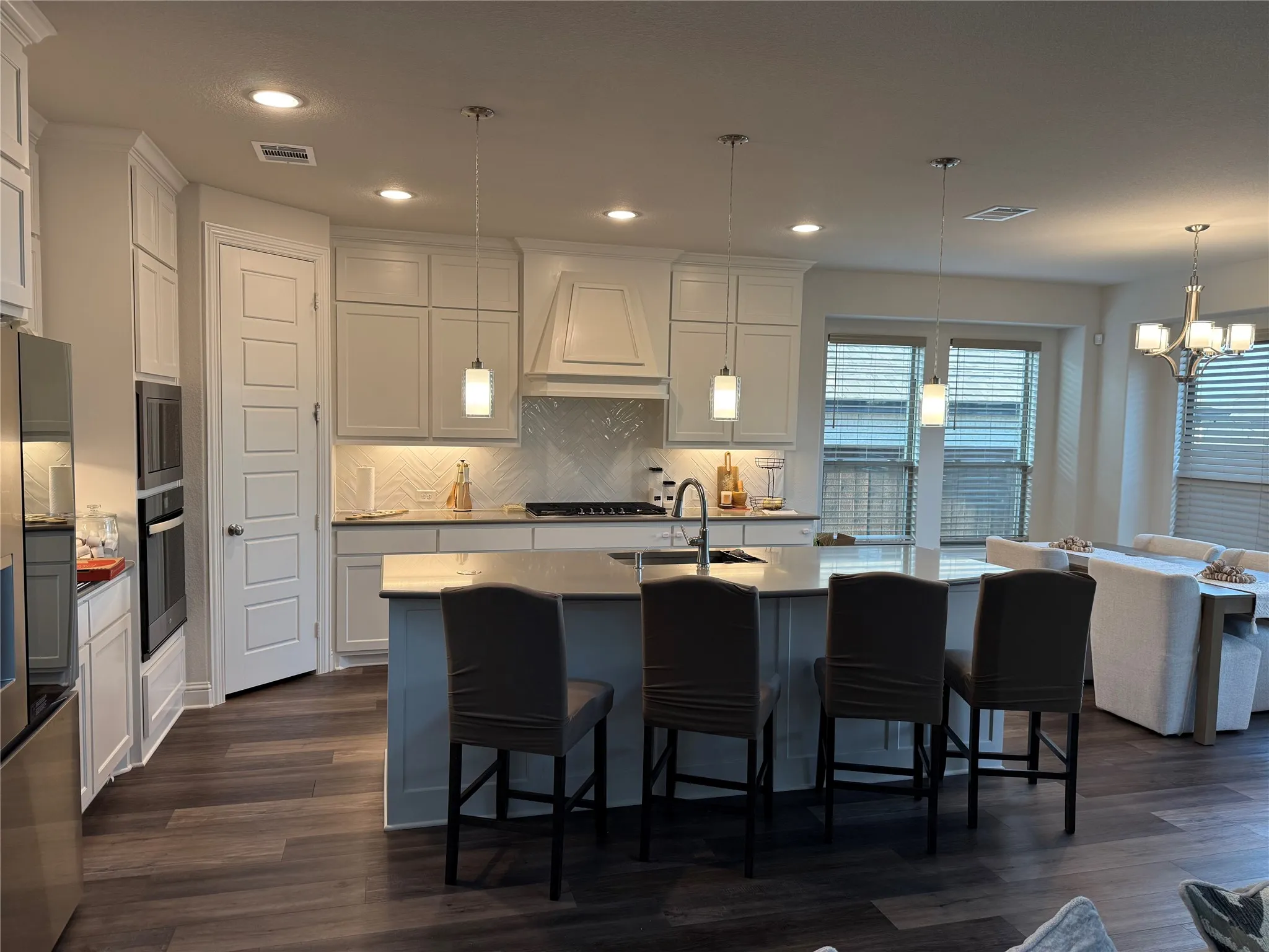 Open-concept kitchen featuring an island with counter seating, stainless steel appliances, white cabinetry, wood-finish flooring, and recessed lighting