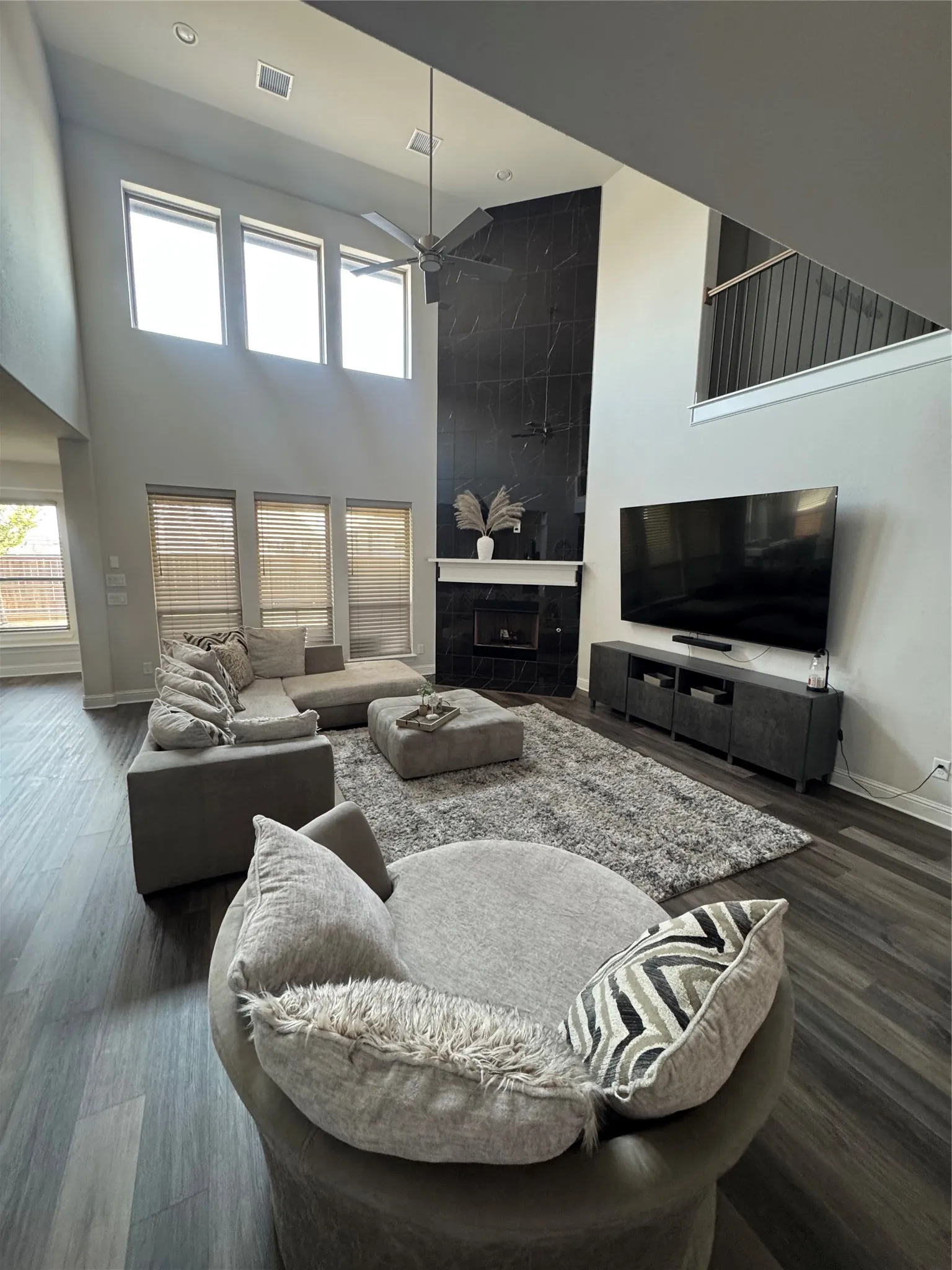 Spacious living area featuring a soaring ceiling, a black stone-finish fireplace with a white mantel, multiple large windows, and dark wood-finish flooring