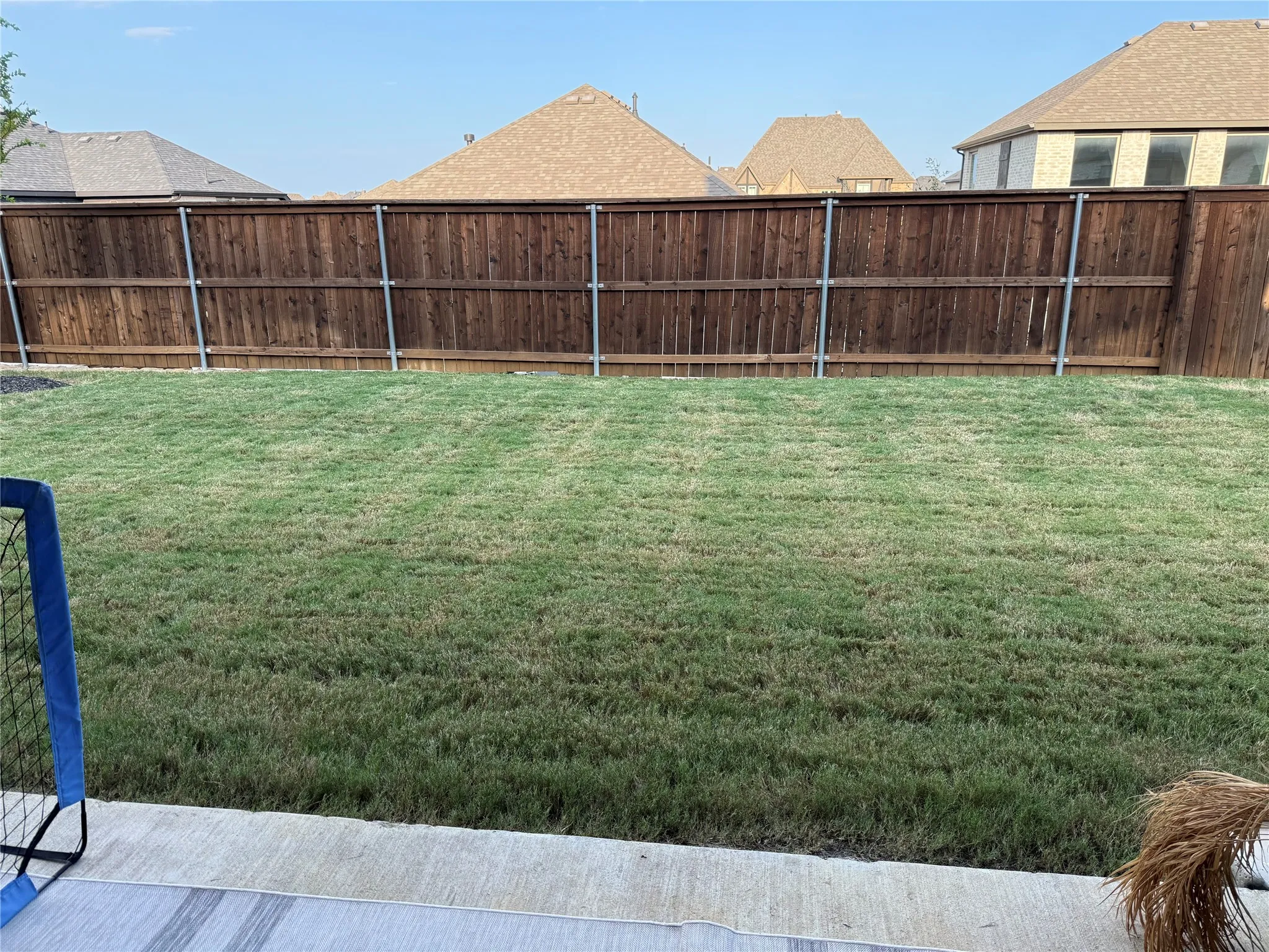 Generous rear yard featuring a wood fence with metal posts, a manicured lawn, and a concrete patio section