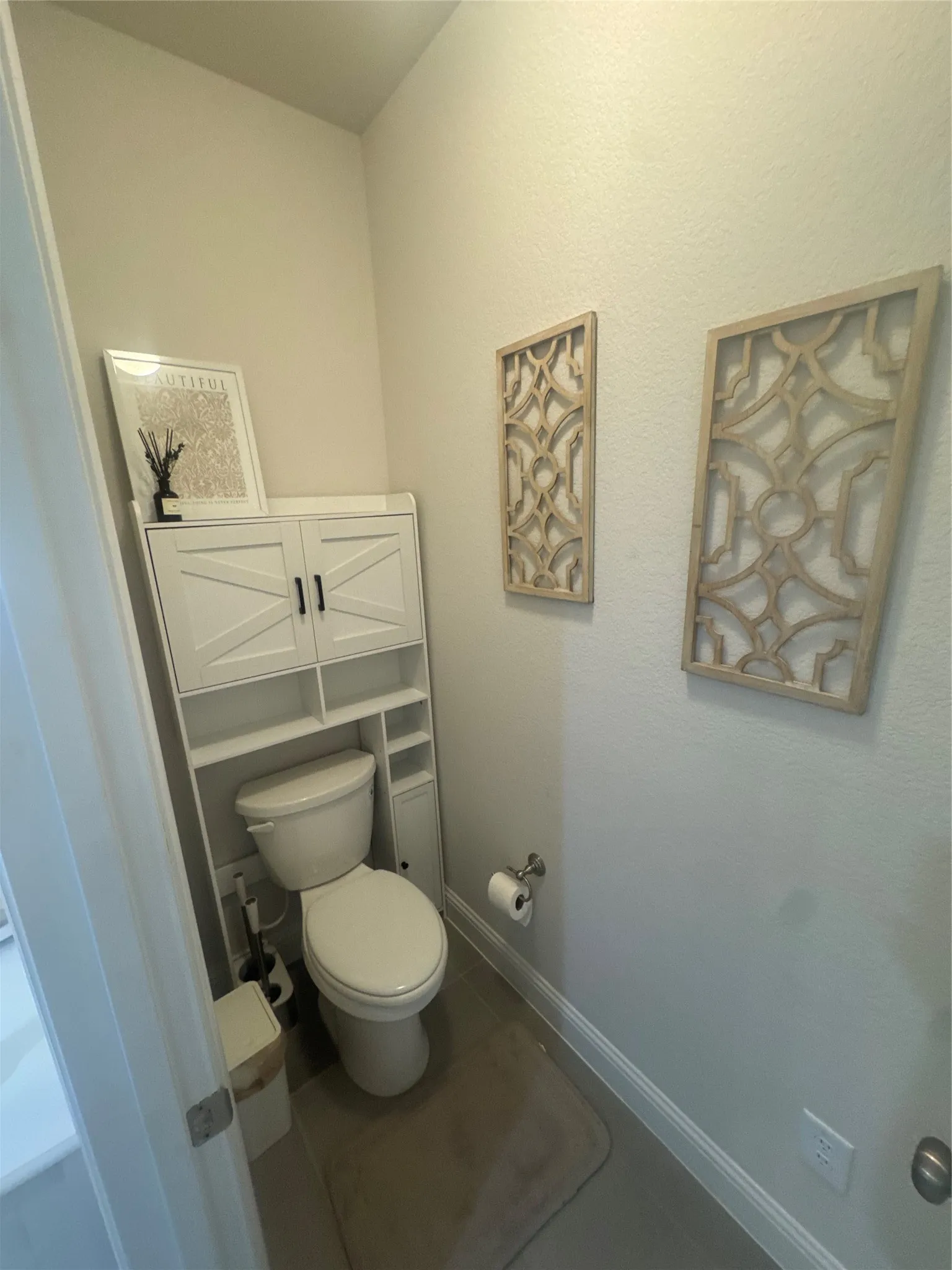 Powder room with a white toilet, white built-in storage cabinet, and light-toned walls