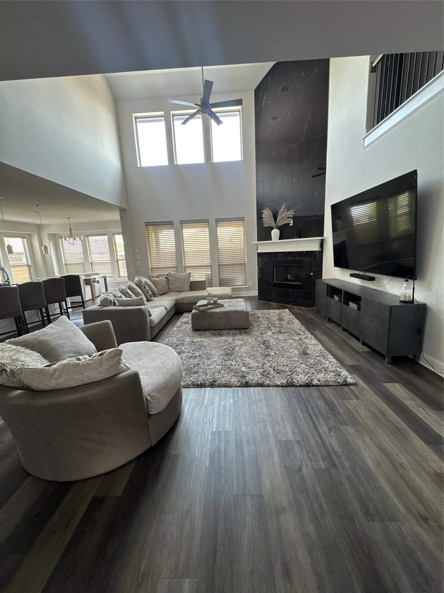Expansive living area featuring a two-story ceiling, wood-finish flooring, and a fireplace with a dark floor to ceiling stone-finish surround