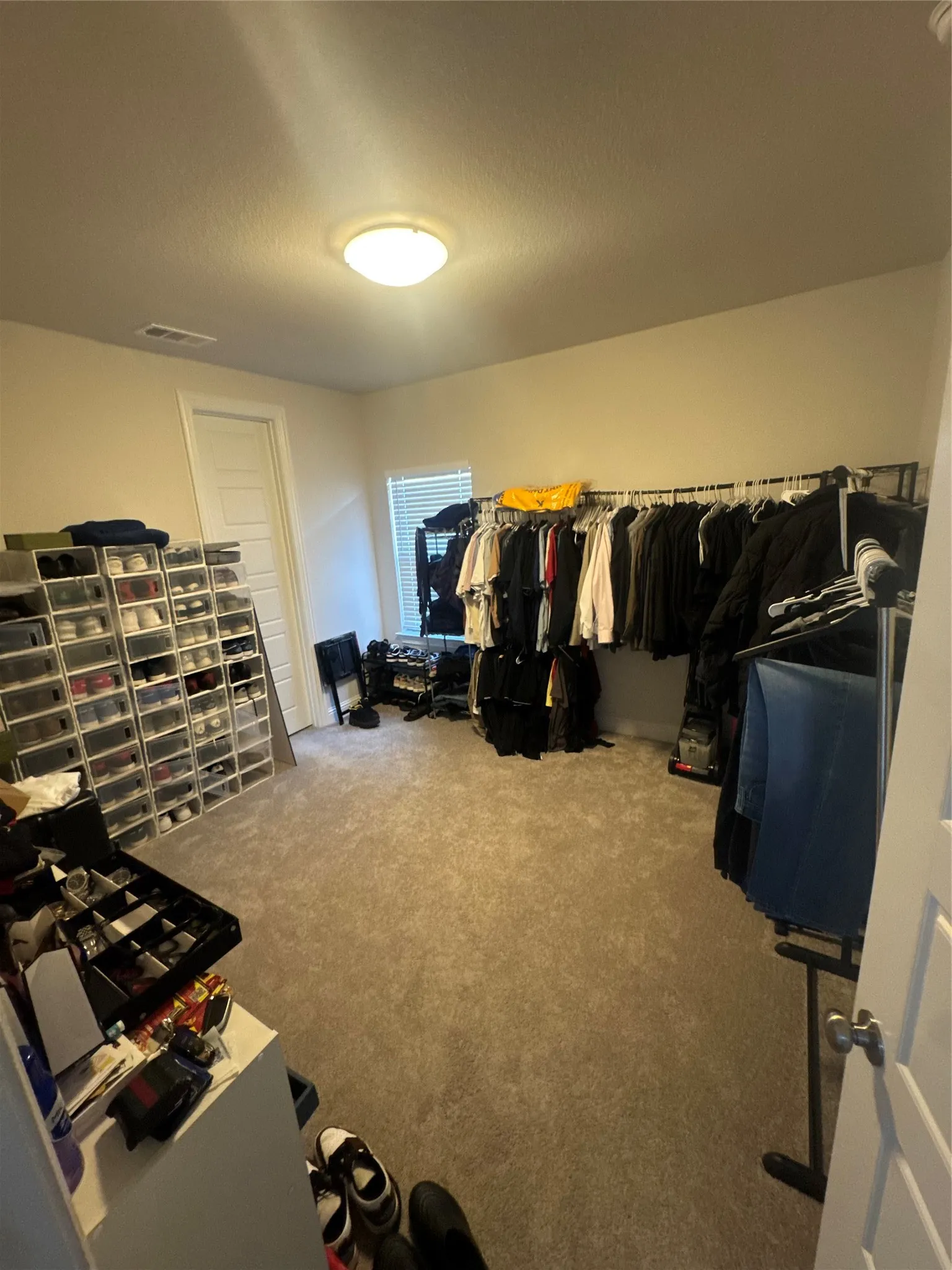 Carpeted room with a ceiling-mounted light fixture, white walls, and a window featuring horizontal blinds- Used as a closet