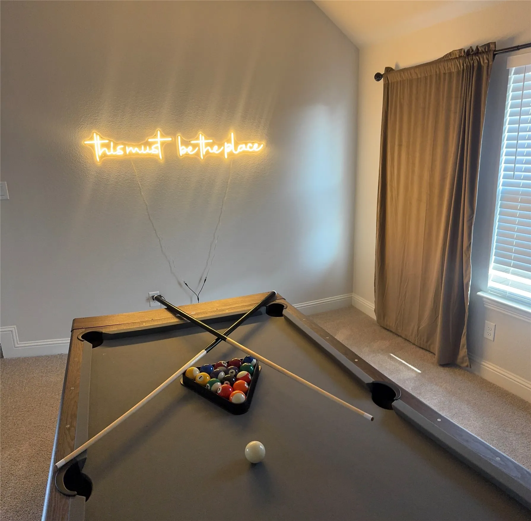 Recreation room featuring a pool table with cues and balls, a window with blinds, and neutral-toned carpeting