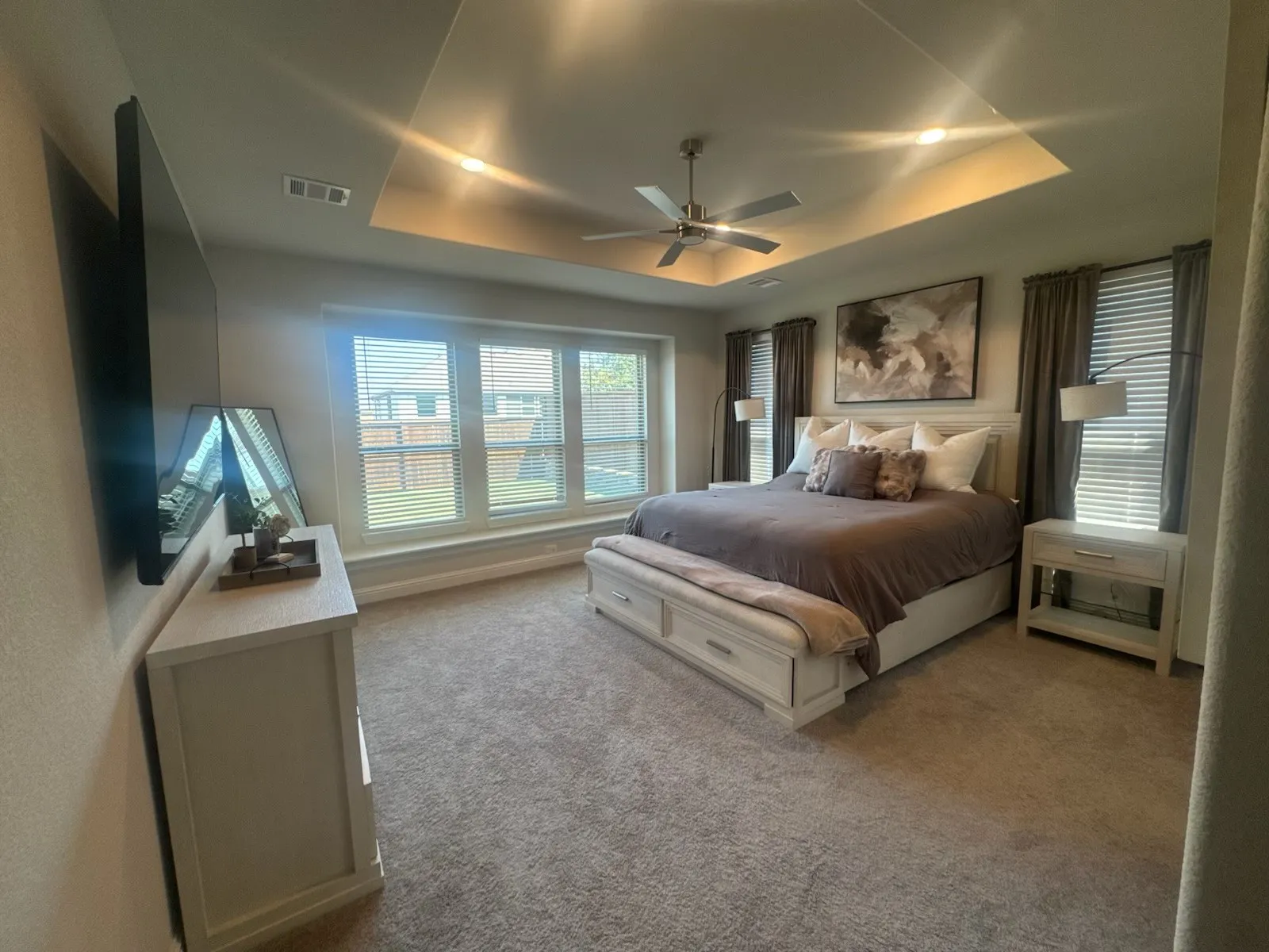 Carpeted bedroom featuring a tray ceiling with recessed lighting, a ceiling fan, and a wall of windows with horizontal blinds