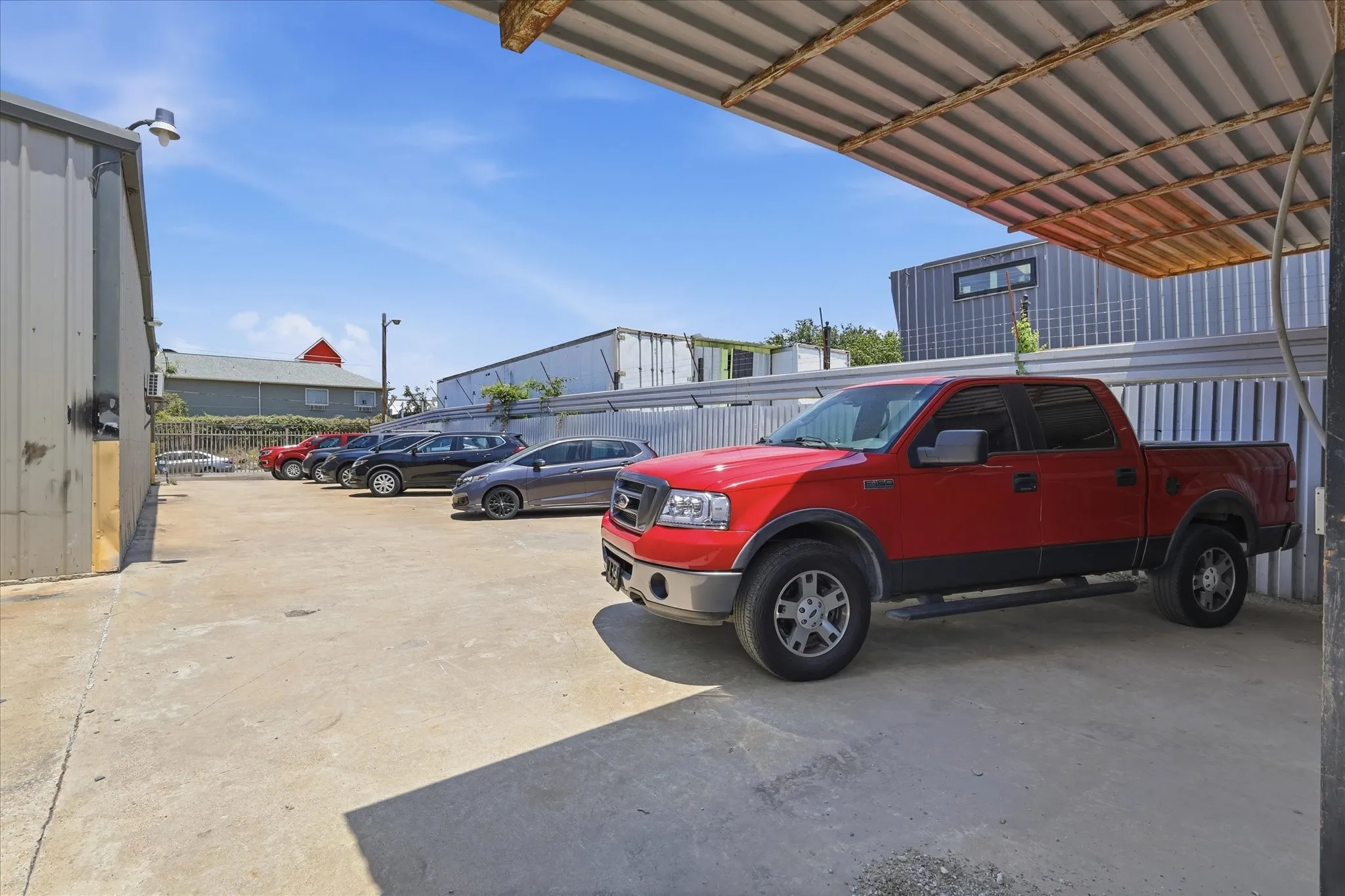 Concrete lot with covered parking structure featuring corrugated metal roofing and a corrugated metal fence