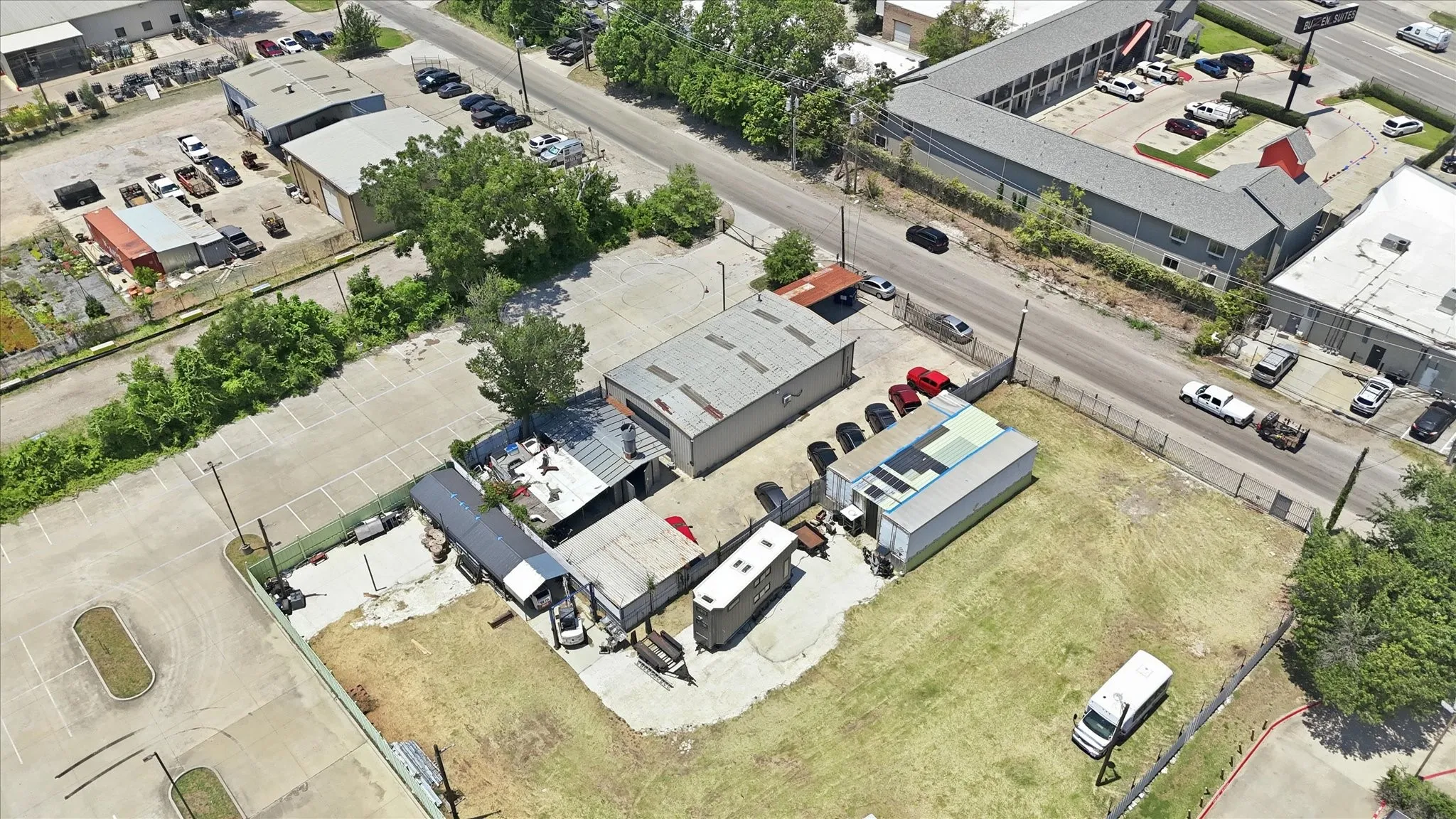 Commercial property featuring multiple structures, paved parking areas, and an expansive grass lot
