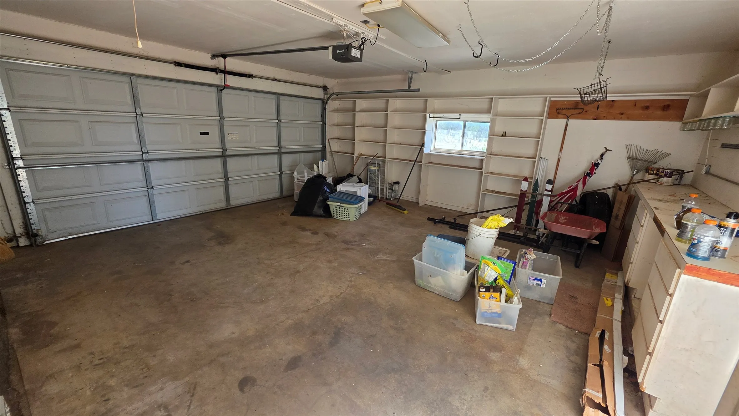 Spacious garage with concrete flooring, two large overhead doors, built-in shelving, a workbench, and a window