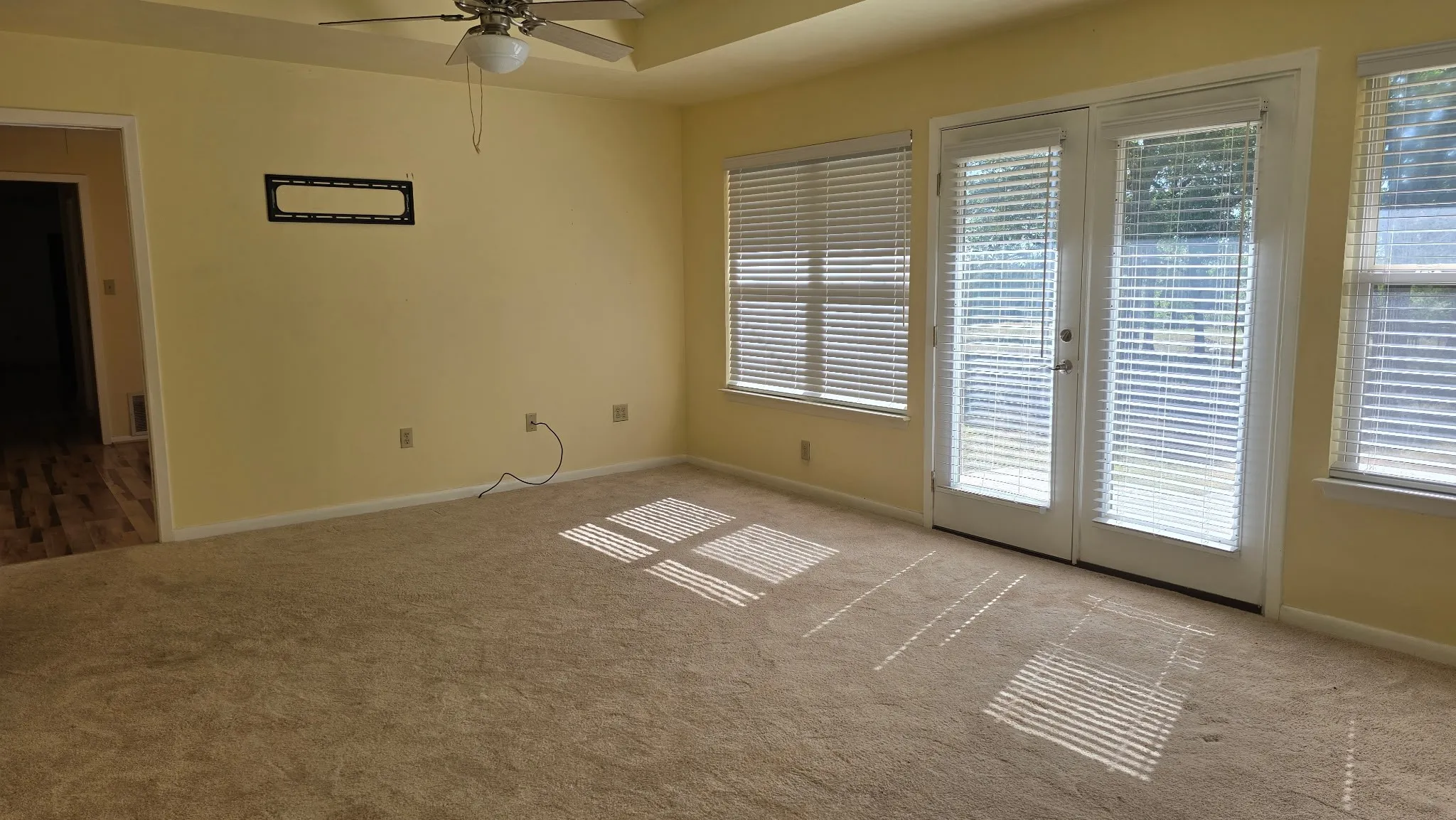 Carpeted room with a ceiling fan, two windows with blinds, and French doors leading to an exterior space