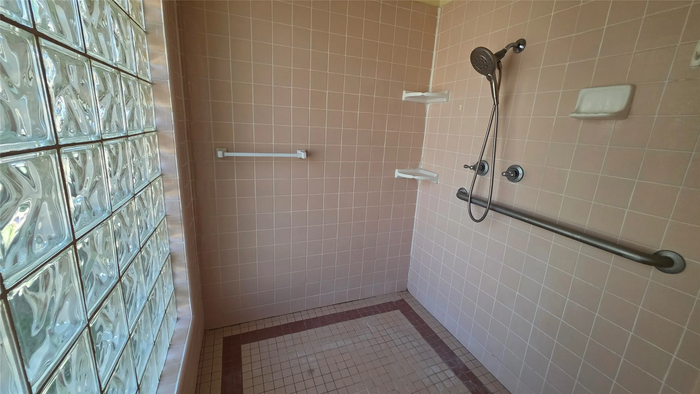 Tiled shower with glass block wall, handheld showerhead, and integrated grab bar