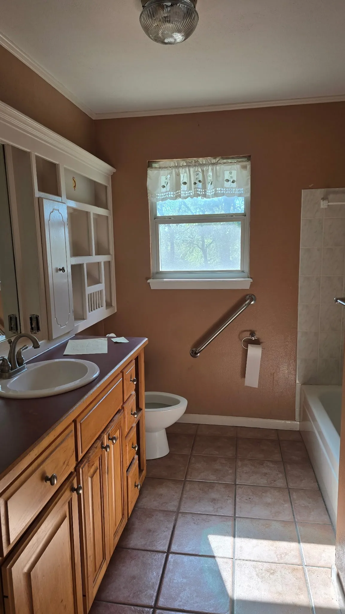 Bathroom featuring a wood-finish vanity with an integrated sink, a built-in storage cabinet, ceramic tile flooring, and a window