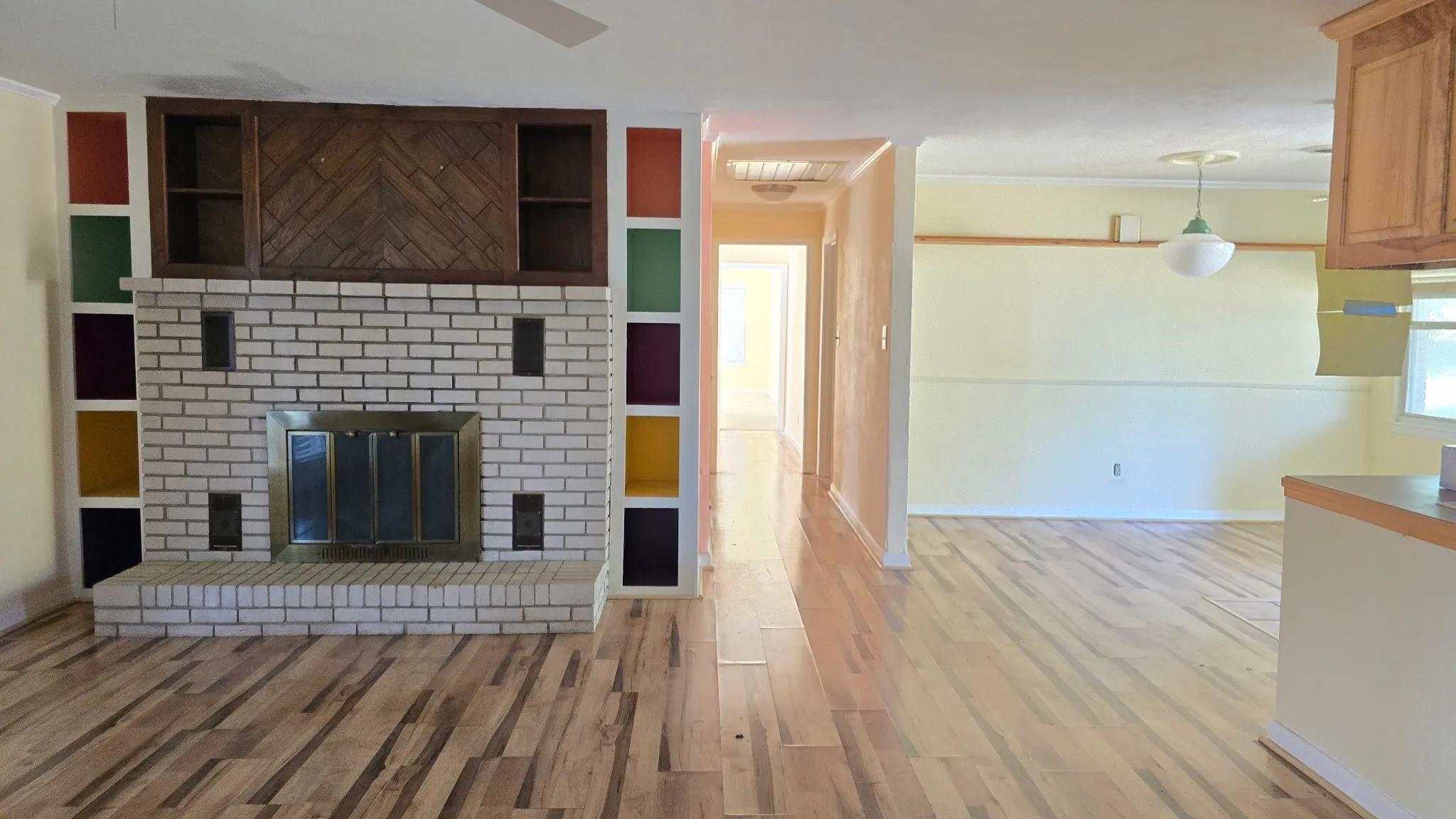 Living area featuring wood-finish flooring, a white brick fireplace with a brass-finish insert, and built-in shelving with colorful accents