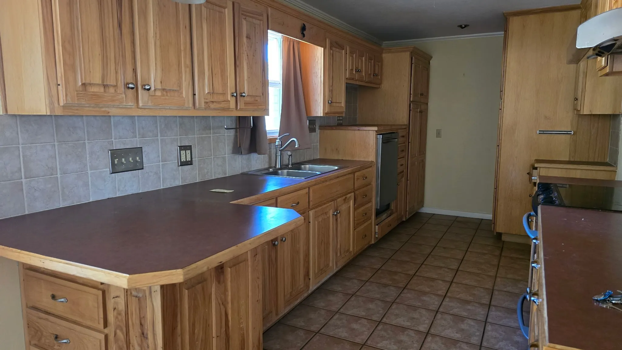 Kitchen featuring extensive wood cabinetry, tile flooring, a tile backsplash, and a double basin sink