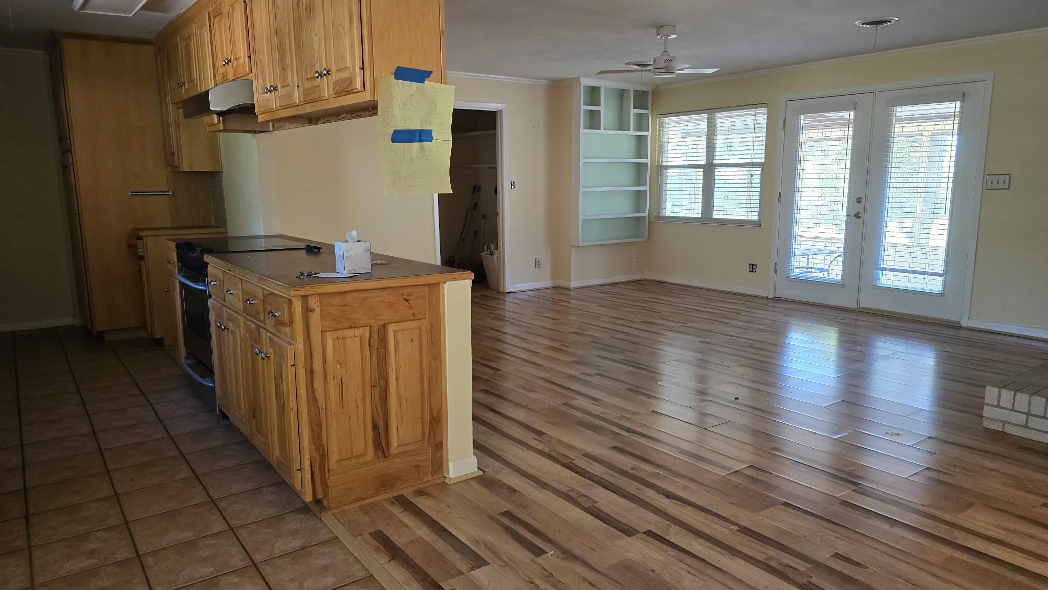 Open-concept living space featuring wood-finish flooring, a kitchen island with built-in cabinetry, dual glass-paneled doors, and a built-in shelving unit
