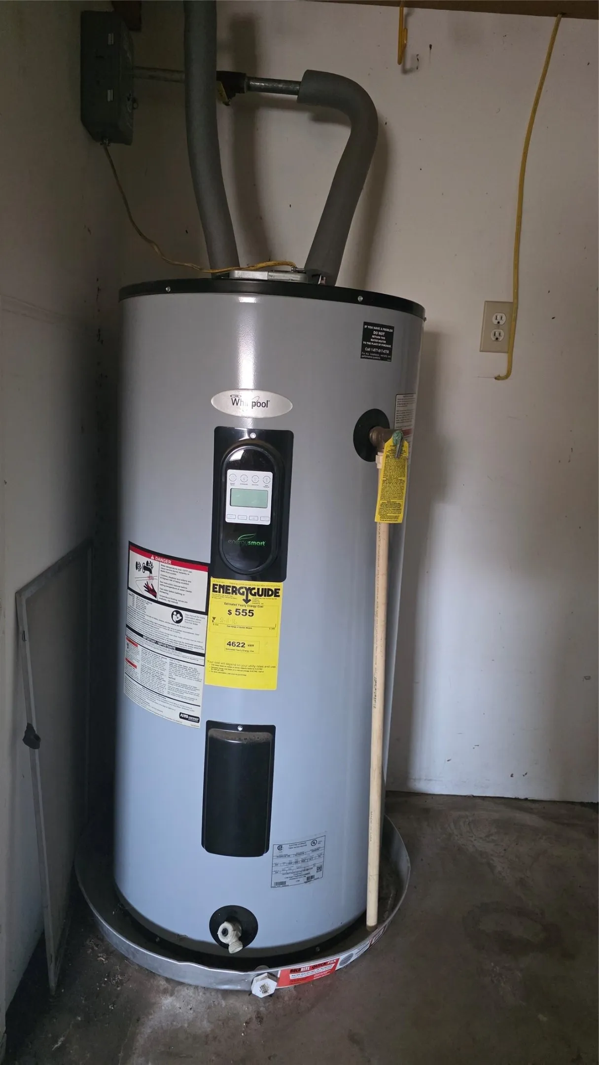 Water heater with a visible energy guide label, seated in a metal drain pan, featuring insulated pipes