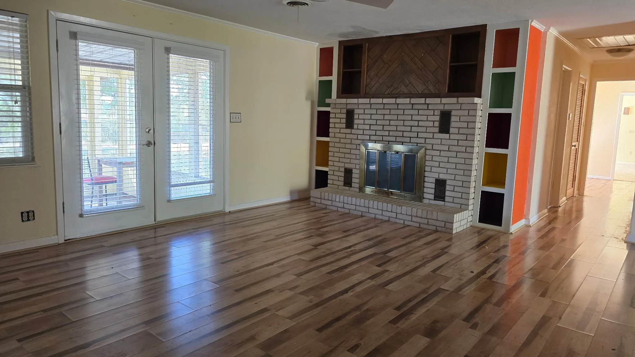 Spacious room featuring wood-finish flooring, a brick fireplace with a brass-finish insert, and built-in shelving with colorful accents
