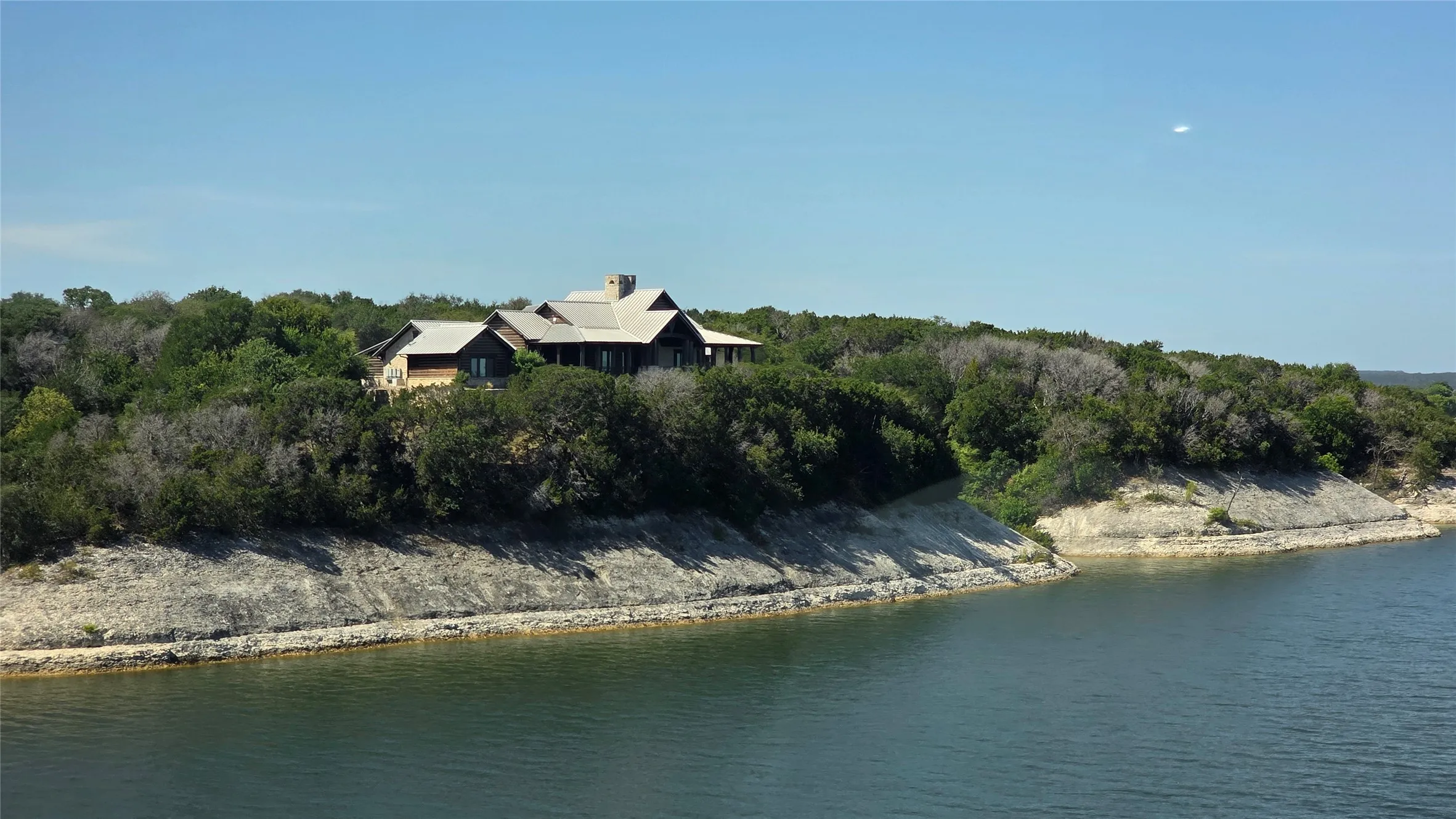 Waterfront property featuring a multi-level residence with a gray metal roof and light-toned siding, set among mature trees
