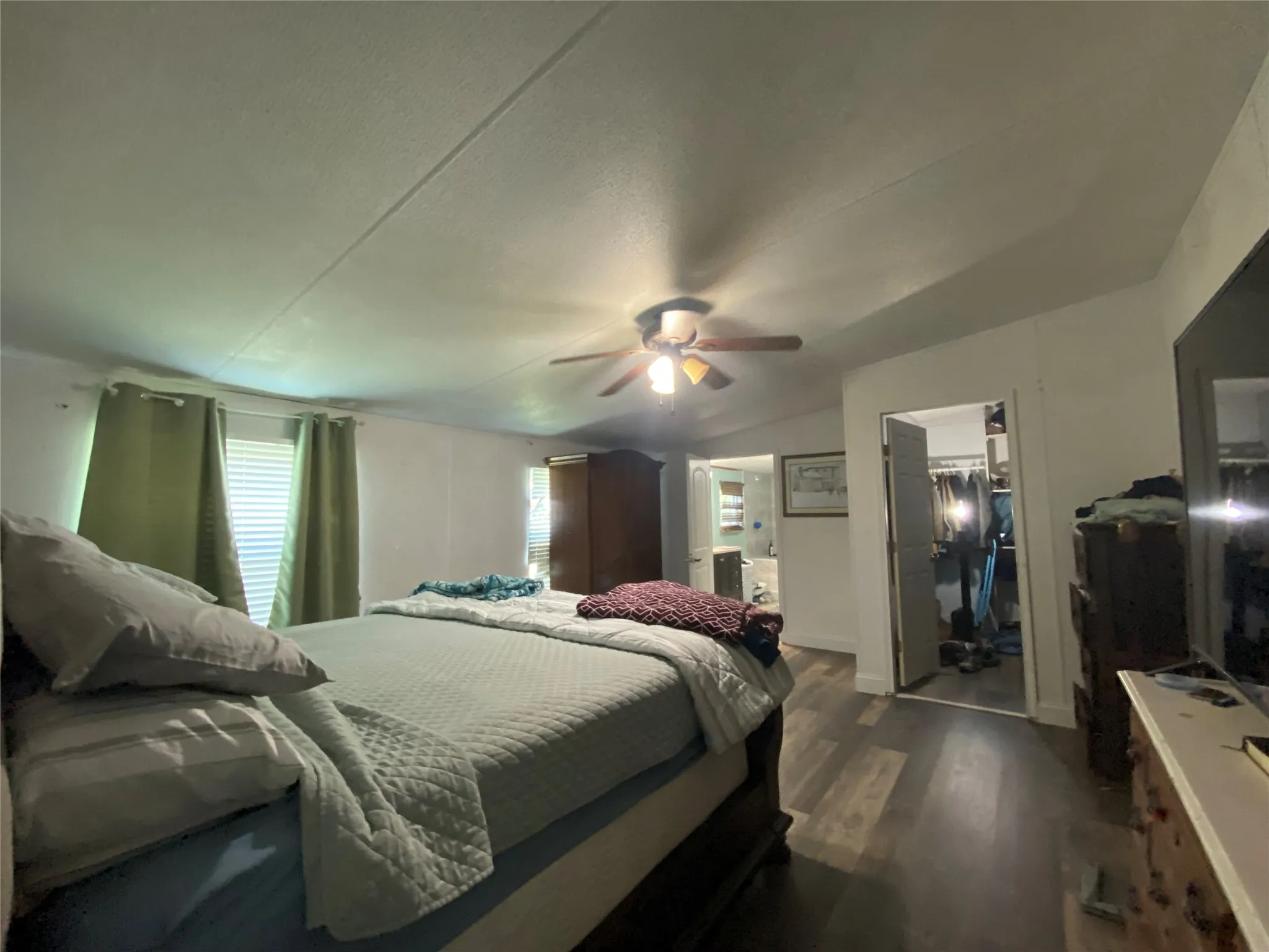 Bedroom with dark wood finished floors, a walk in closet, vaulted ceiling, ceiling fan, and a textured ceiling