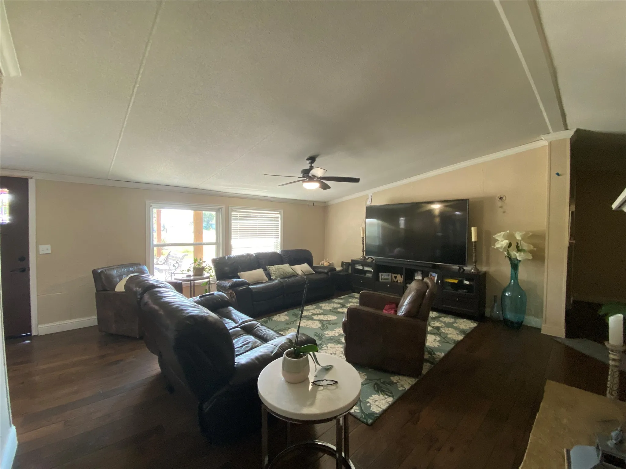 Living room with ornamental molding, dark wood-type flooring, vaulted ceiling, and a ceiling fan