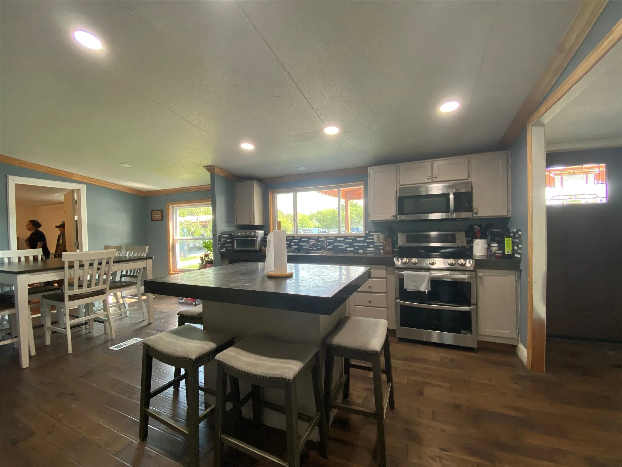Kitchen featuring tasteful backsplash, appliances with stainless steel finishes, dark countertops, ornamental molding, and dark wood finished floors